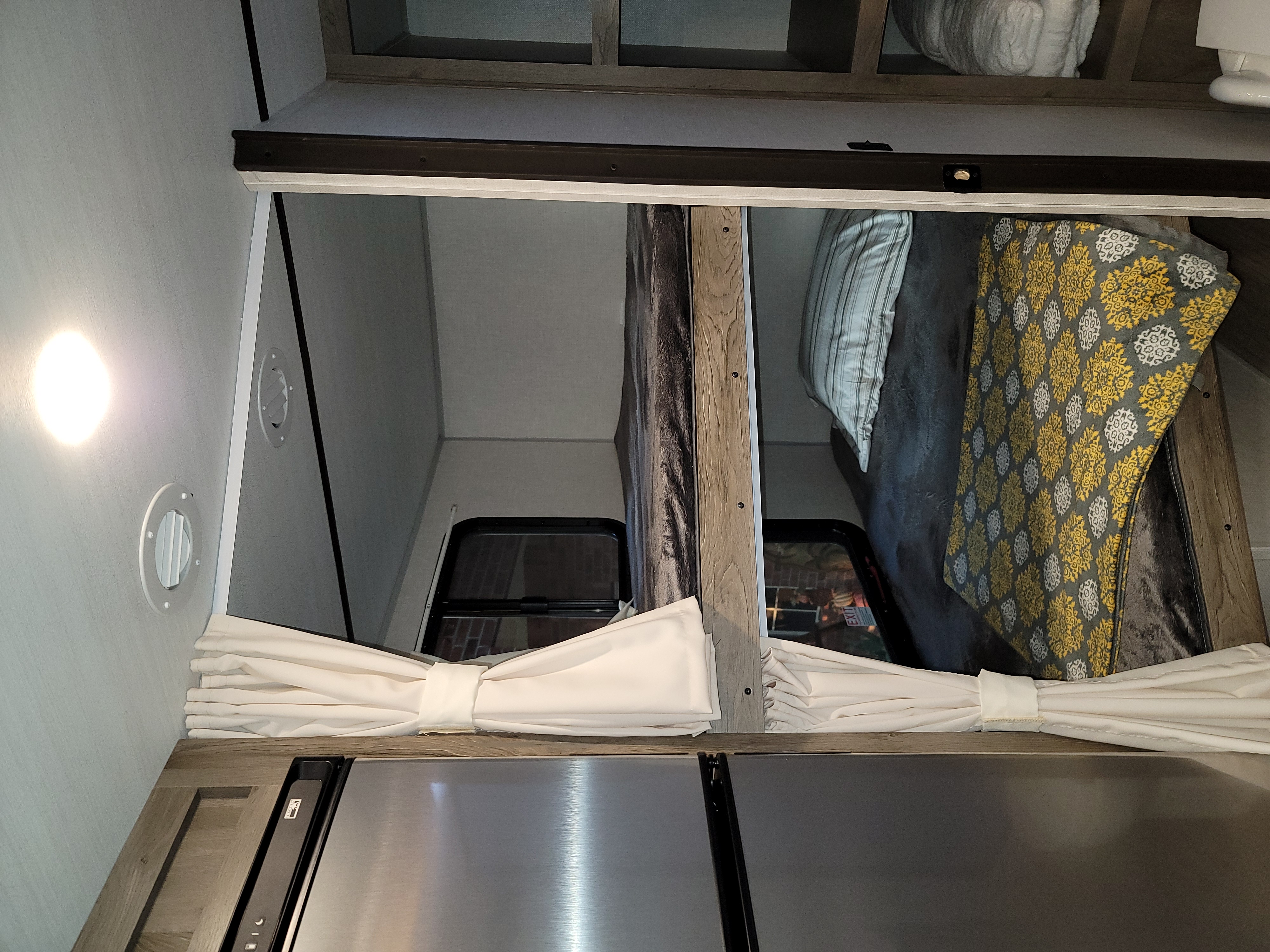 Cozy interior of an RV rental: stacked bunk beds with bedding, a window, and a refrigerator below. Light fixtures, vents, and tied-back curtains are visible.. Forest River Surveyor 2021
