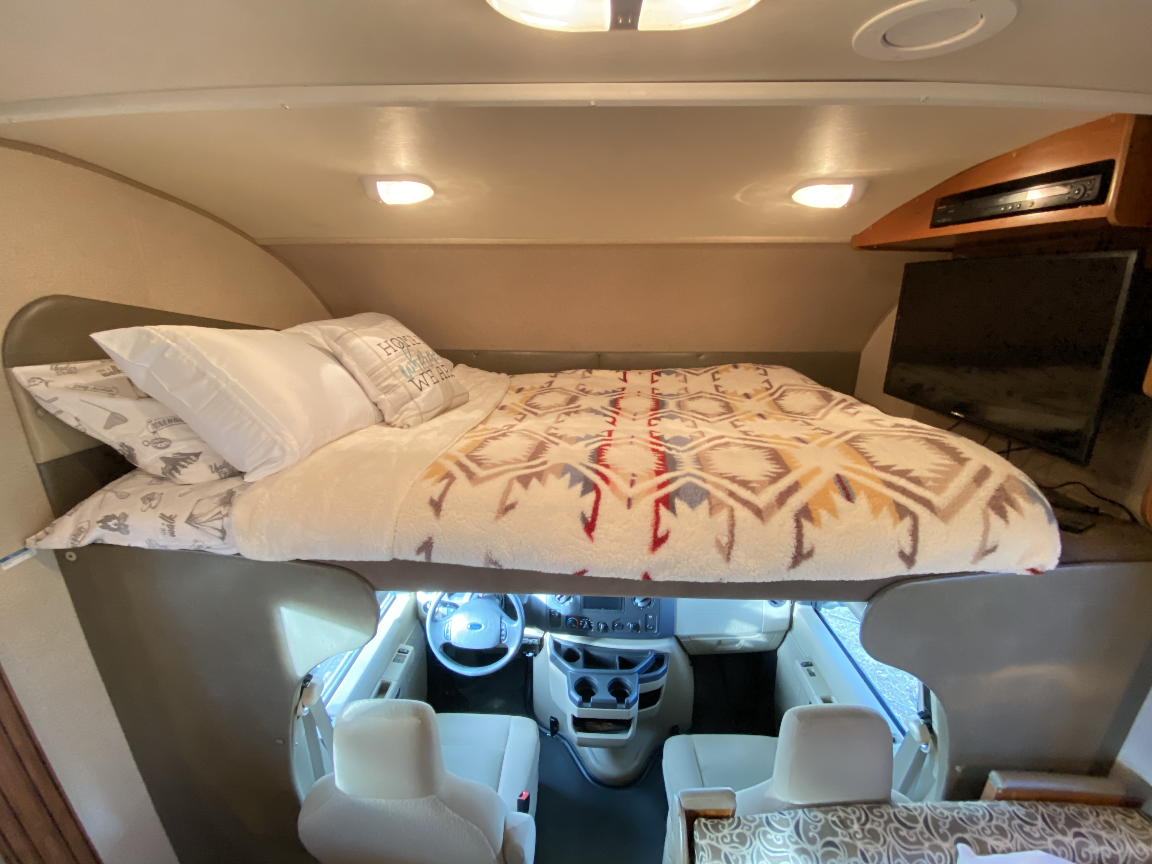Cozy sleeping area in this RV rental, with a bed positioned above the driver's cabin. TV is visible on the right.. Jayco Redhawk 2016