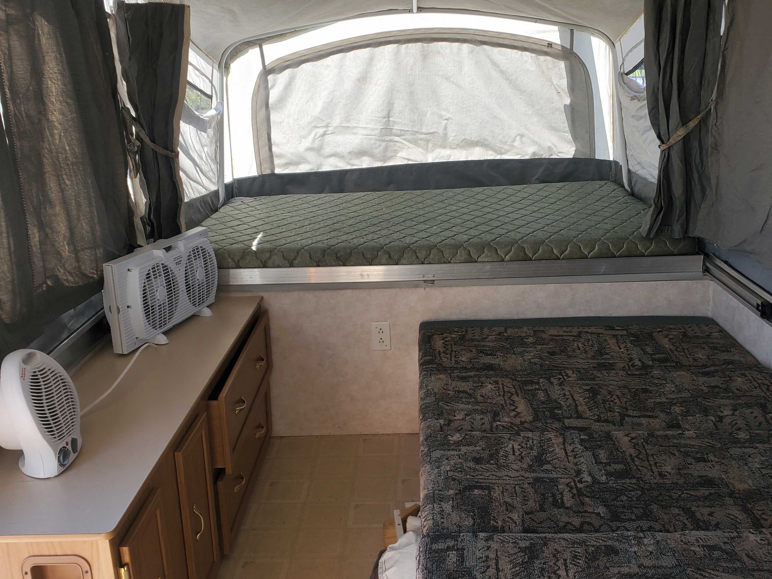 RV rental pop-up camper interior: featuring a raised green bed, patterned seating, fans, and storage cabinets.. Fleetwood Sana Fi Colman 1999