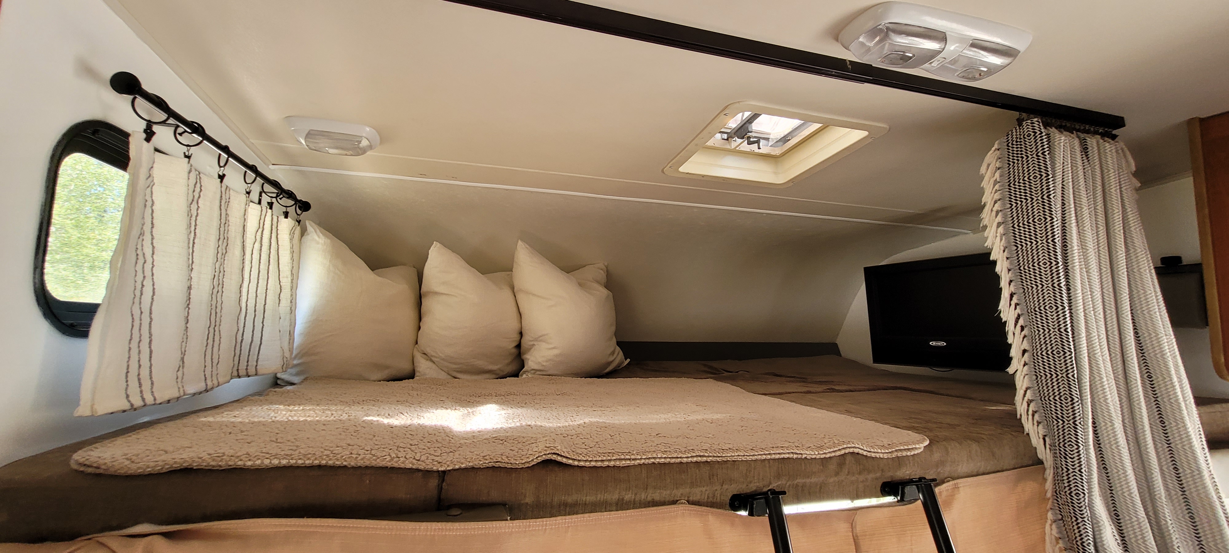 RV rental cab-over bed features cozy bedding, window, TV, skylight, and decorative privacy curtains.. Other Freelander 2011
