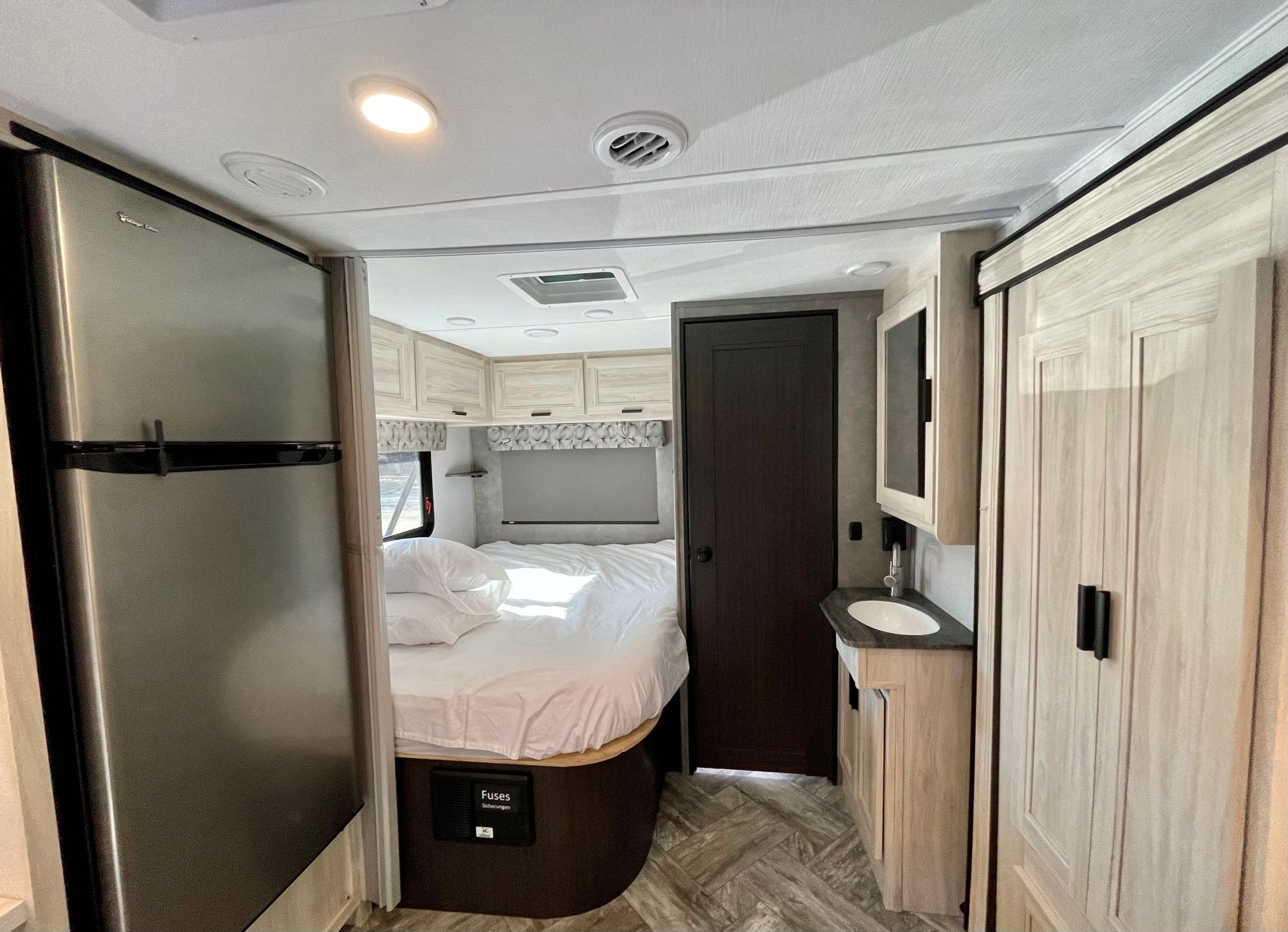 RV rental's functional interior: cozy bed, full-size fridge, and bathroom vanity, offering a complete travel living space.. Forest River Sunseeker 2022