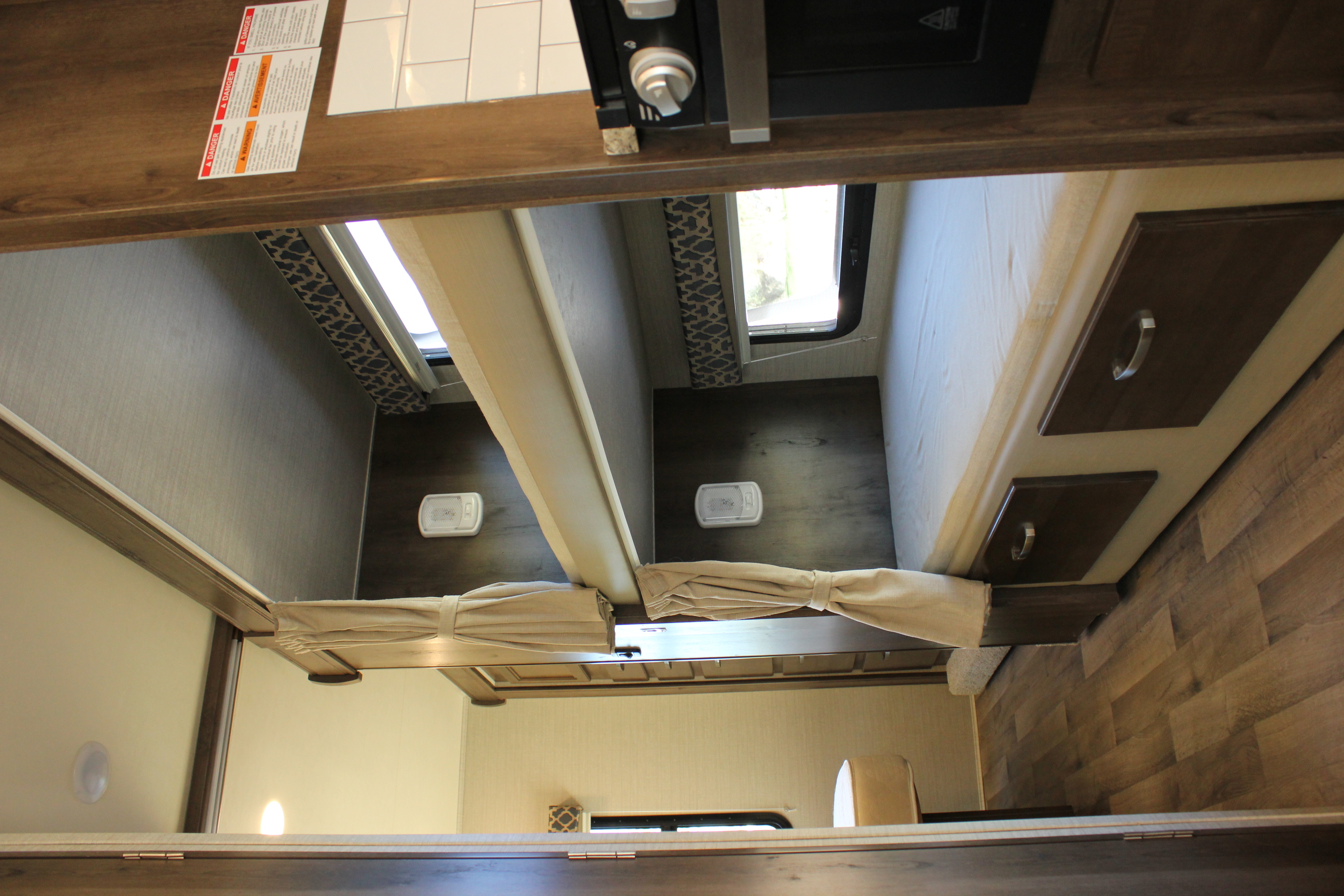 Looking into an RV rental, showing compact bunk beds with windows, storage drawers, and a partial view of the kitchen counter.. Jayco Redhawk 2020