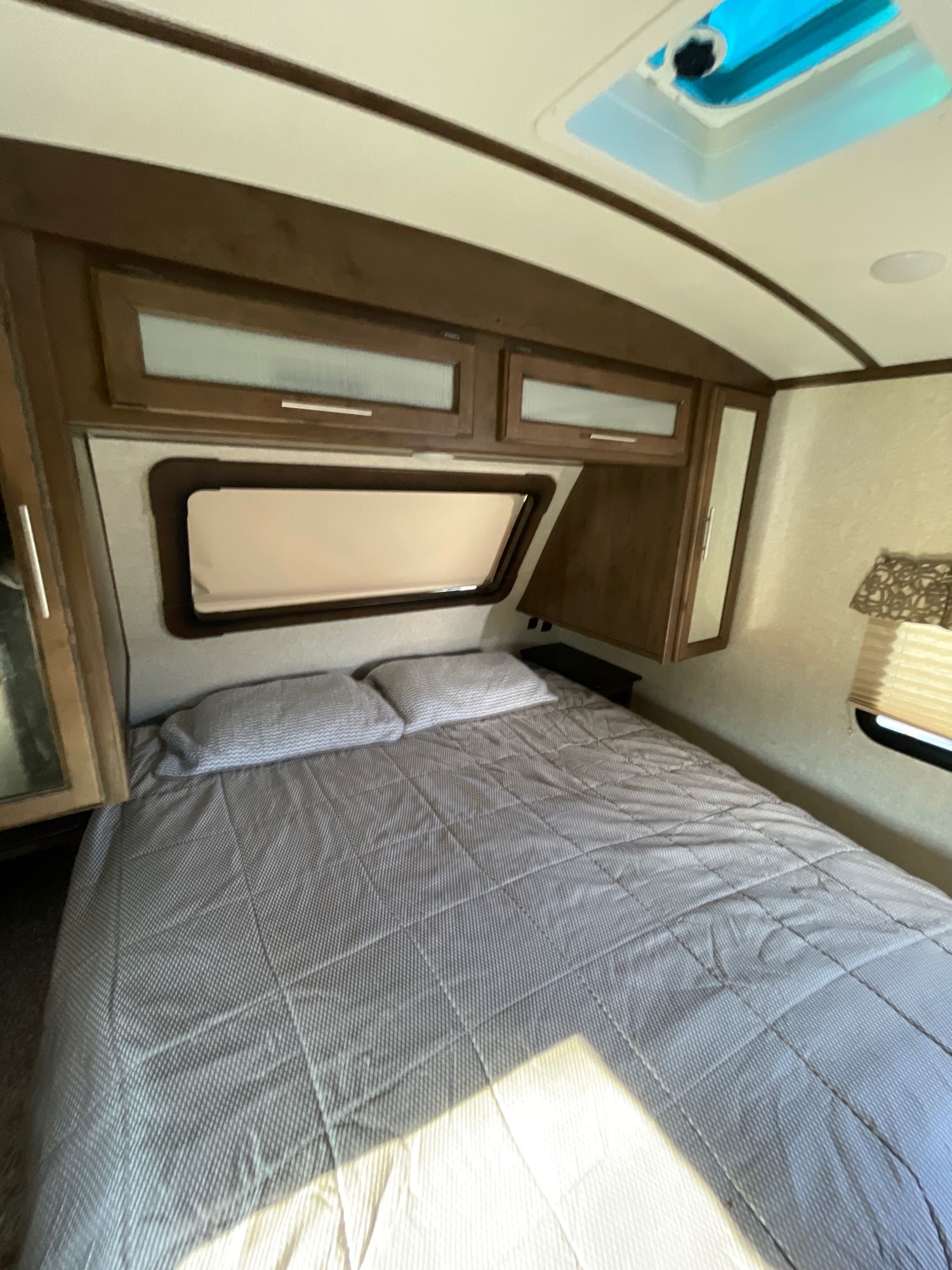 Cozy RV rental bedroom featuring a patterned bed, overhead cabinets, and a bright skylight. Perfect for your next adventure.. Keystone Cougar Half-Ton 2019