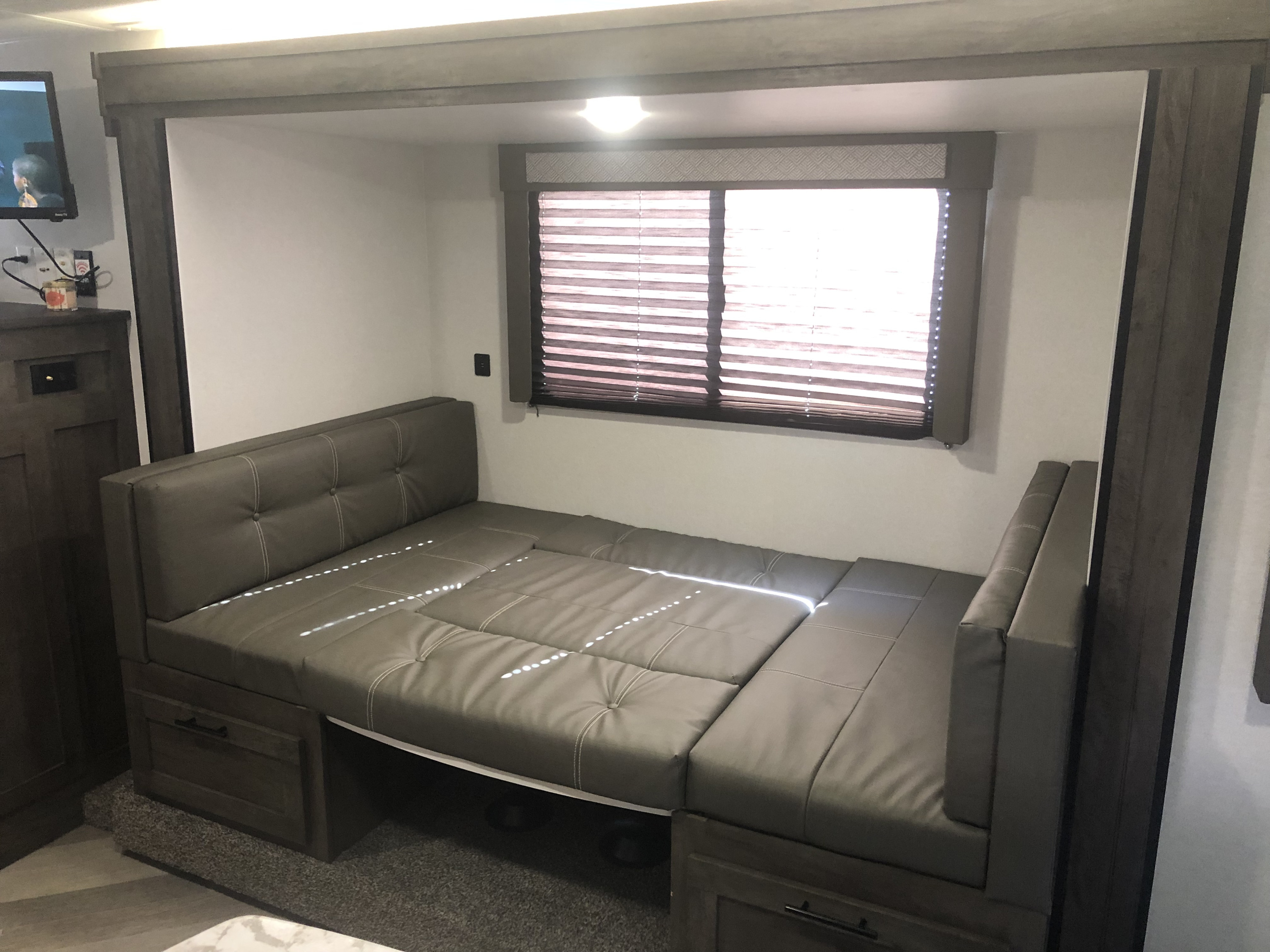 Inside an RV rental: a modern, grey convertible sofa/bed, ideal for compact living and sleeping, beside a window with blinds.. Forest River Salem Cruise Lite 2020