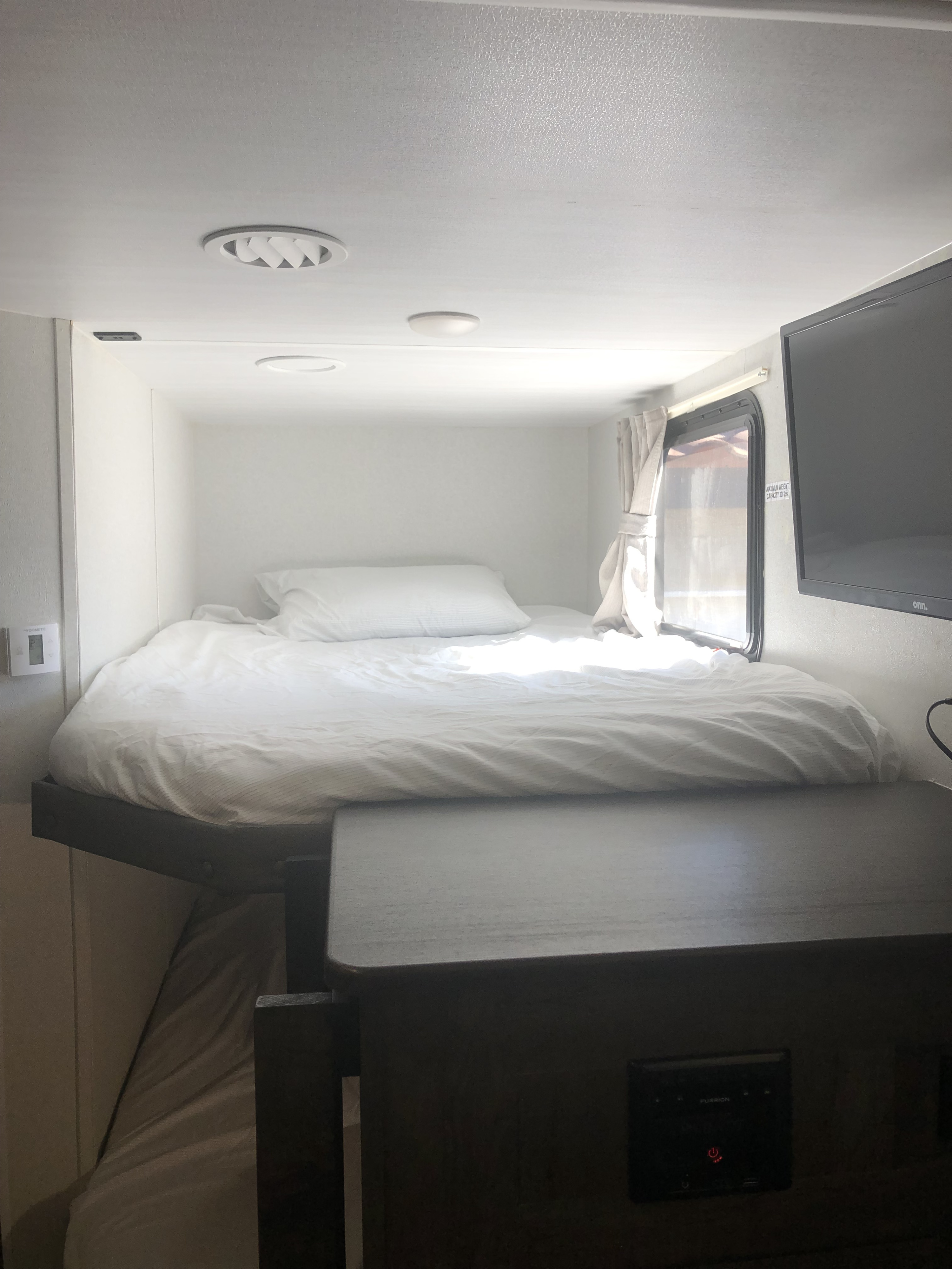 Bright RV rental bedroom area with an elevated bed, white linens, window, wall-mounted TV, and a lower table.. Forest River Salem Cruise Lite 2020