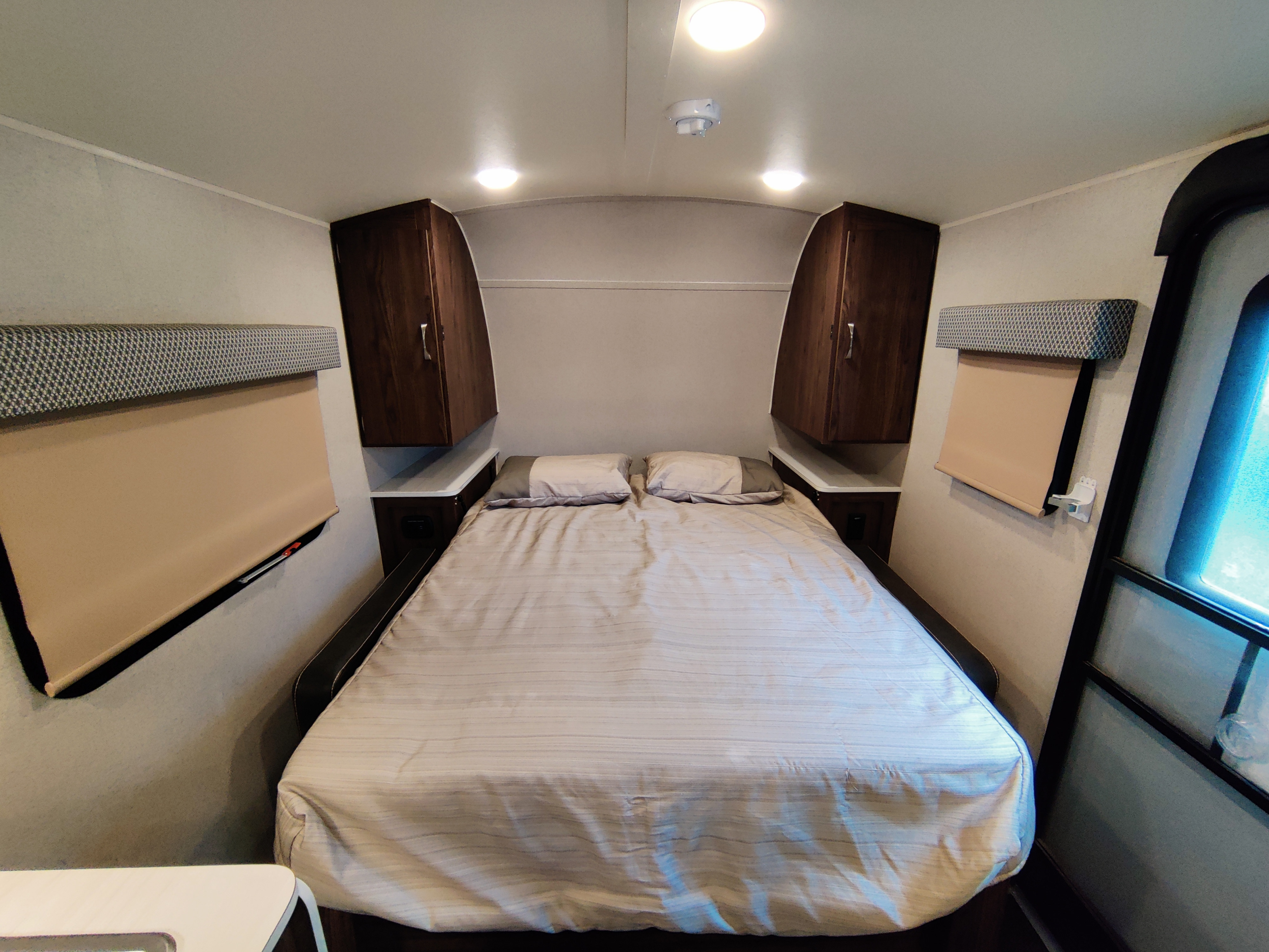 Cozy RV rental bedroom featuring a queen bed with striped bedding, overhead storage cabinets, and pull-down window shades.. Forest River Geo Pro 2018