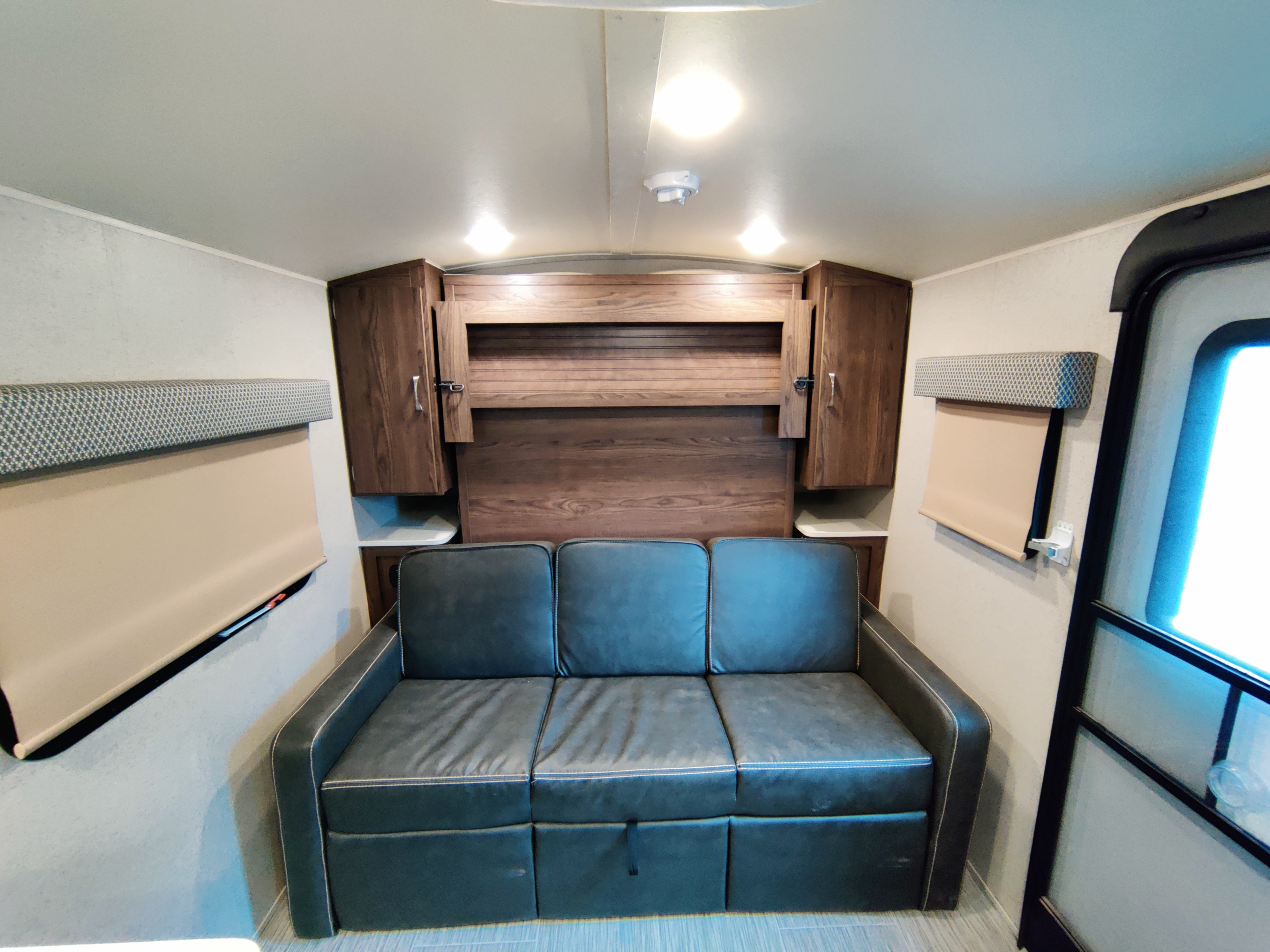 RV rental interior with a dark sofa, wooden overhead cabinets, and window blinds, offering cozy living space for travelers.. Forest River Geo Pro 2018