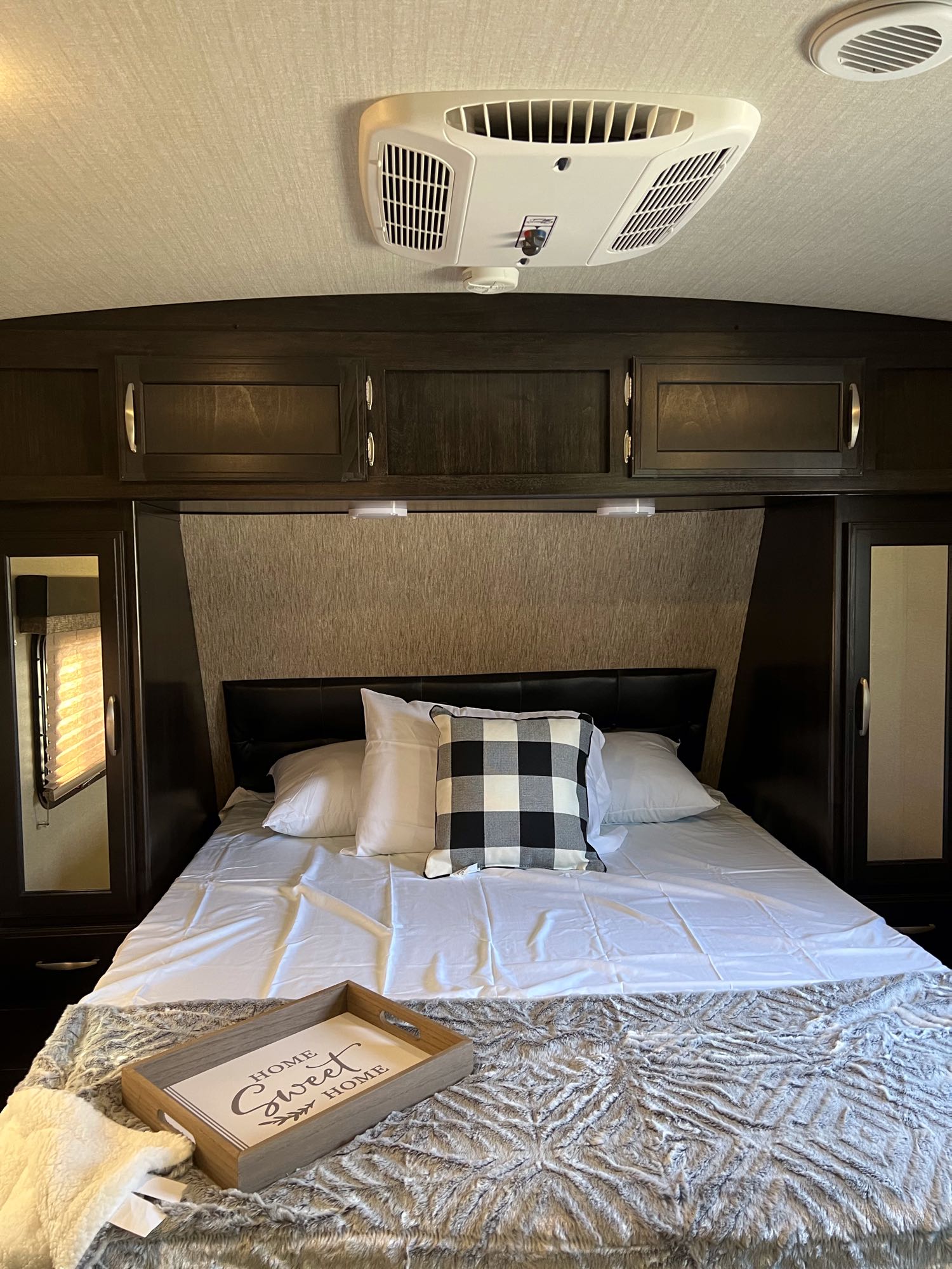 Cozy RV rental bedroom with comfortable bedding and overhead AC. Features wood cabinets and a "Home Sweet Home" tray.. Grand Design Imagine 2018
