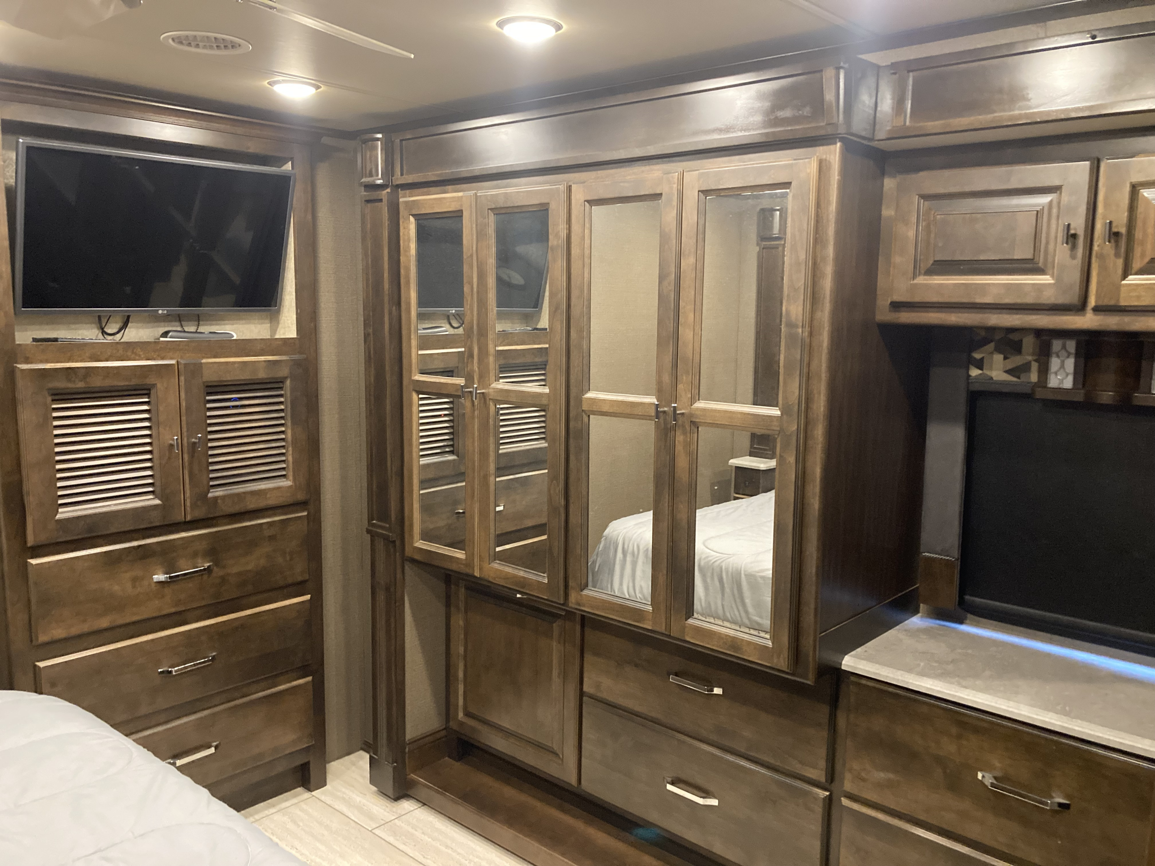 Modern RV rental bedroom featuring a large TV, ample built-in storage, and a mirrored wardrobe for comfortable living.. Allegro Allegro Open Road 2018