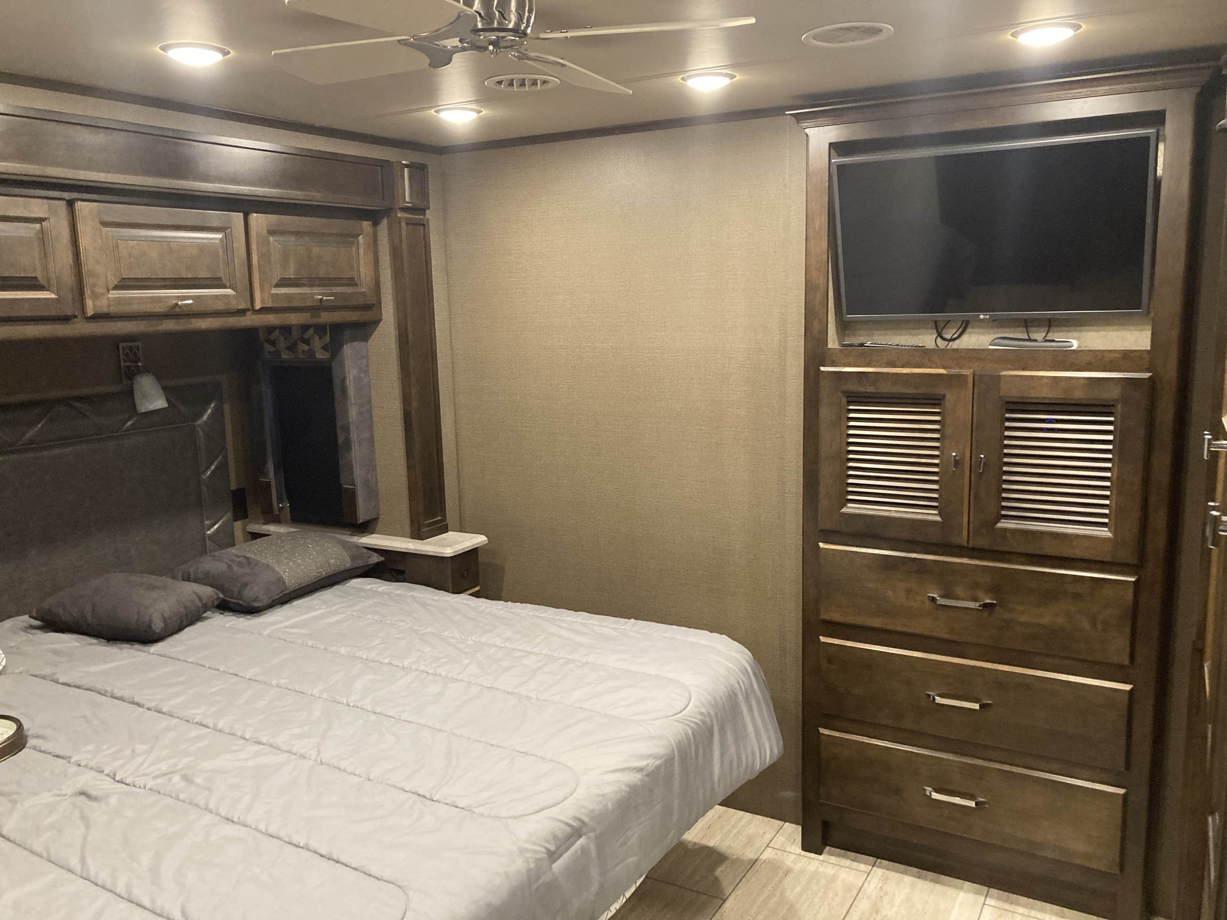 RV rental bedroom view: comfortable bed, overhead cabinets, wall-mounted TV, and ceiling fan.. Allegro Allegro Open Road 2018