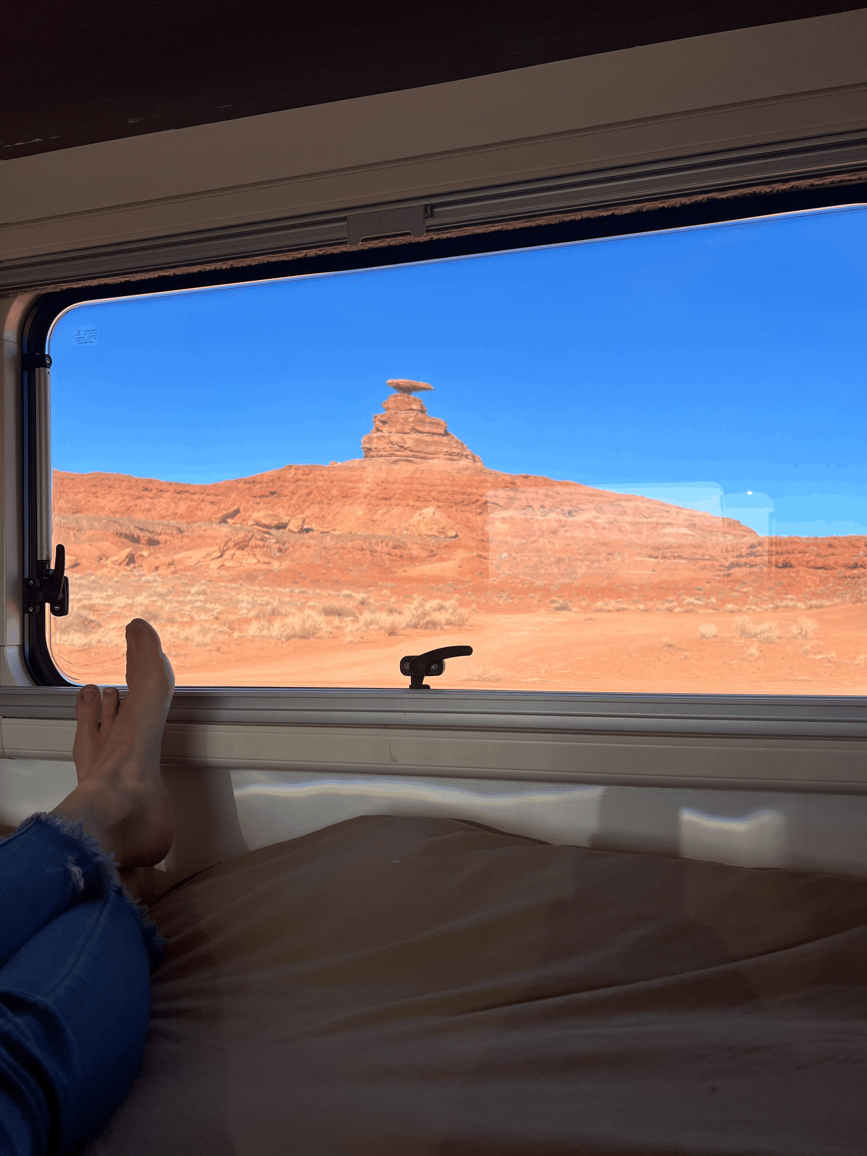 Relaxing inside an RV rental, feet up, enjoying a unique balanced rock formation in the red desert under a clear blue sky.. Winnebago View 2016