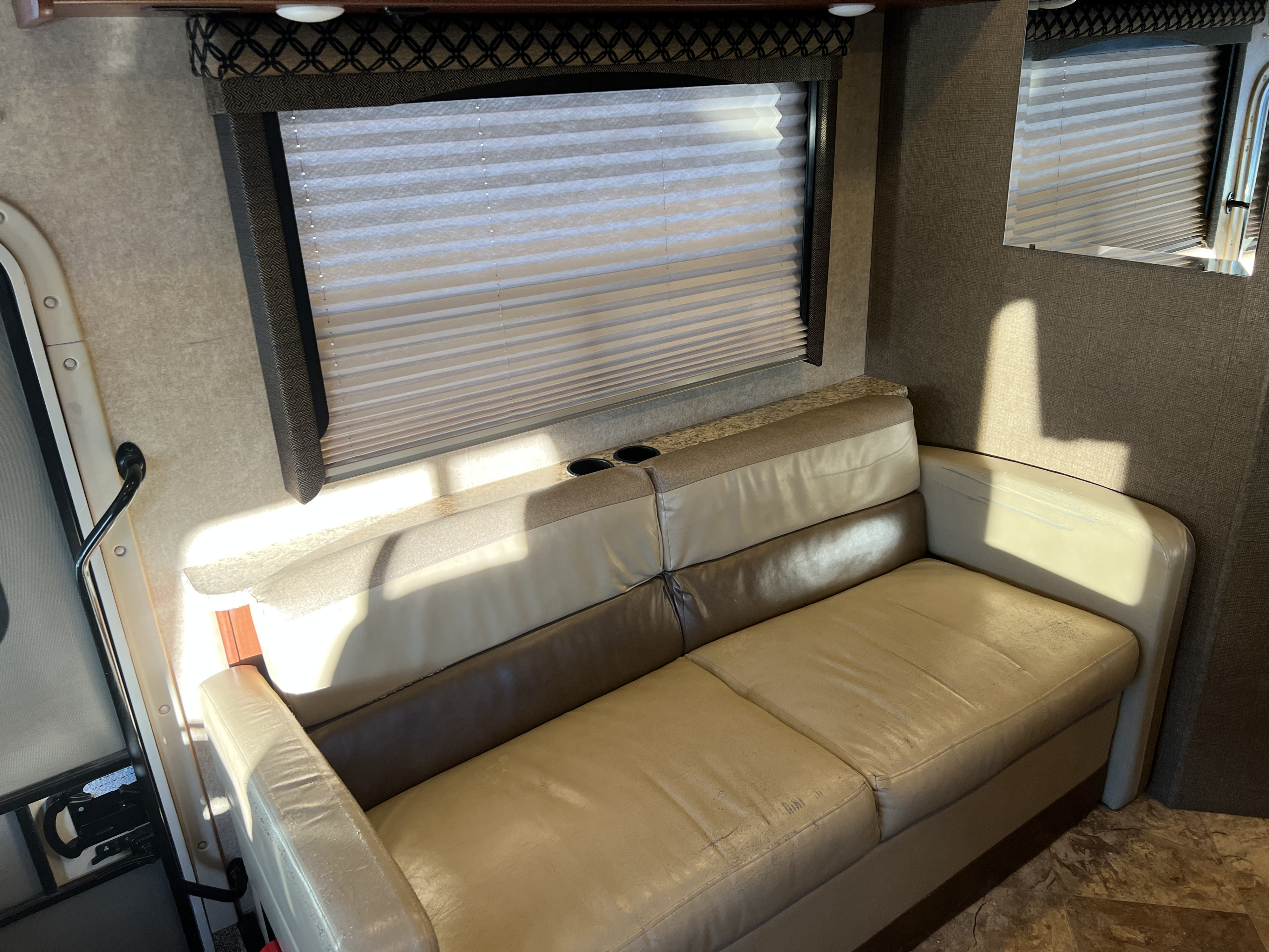 RV rental's cozy interior featuring a light sofa with cupholders and window blinds, illuminated by sunlight.. Thor Motor Coach A.C.E 2017