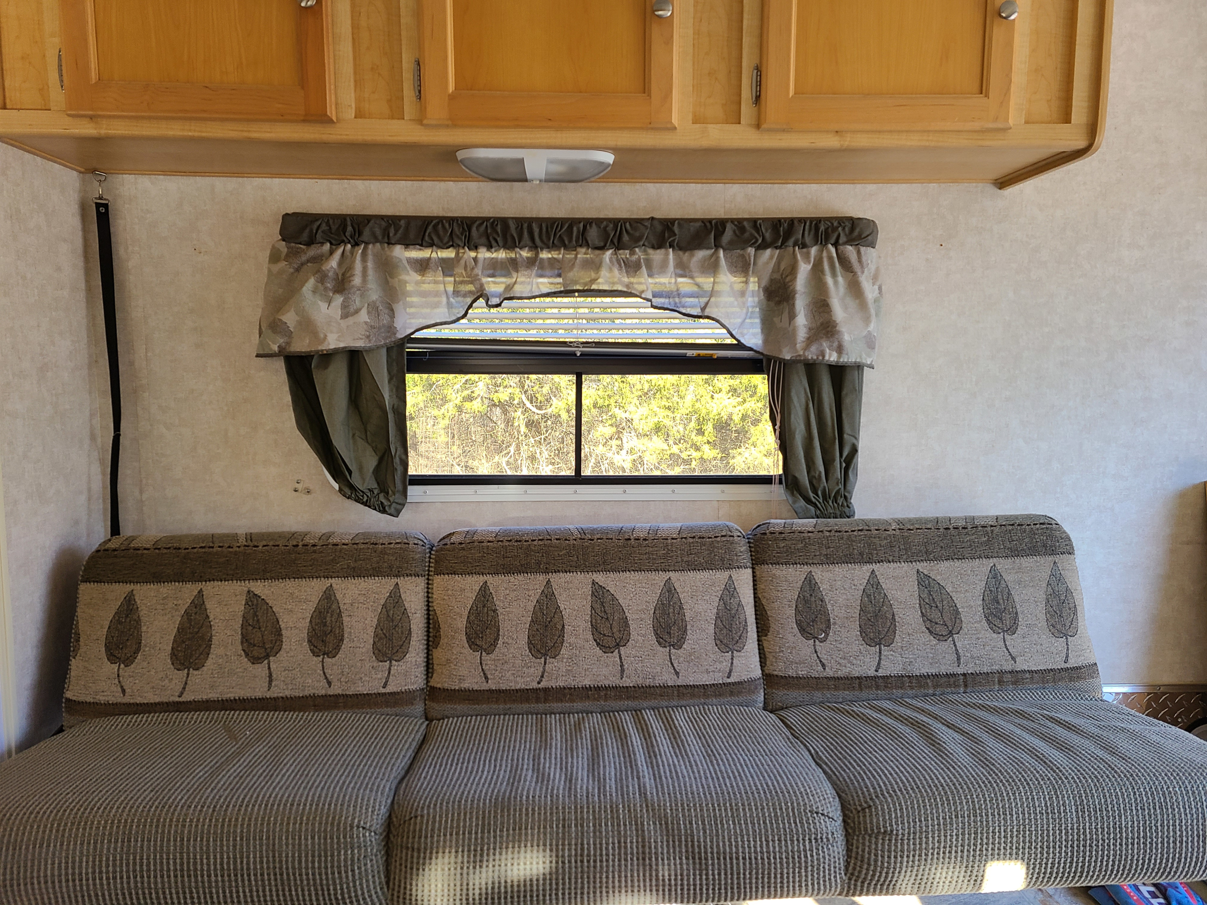 RV rental interior featuring a three-section sofa with leaf-patterned backs, wooden cabinets, and a window with blinds and valance.. R-Vision R-Wagon 291rw 2006