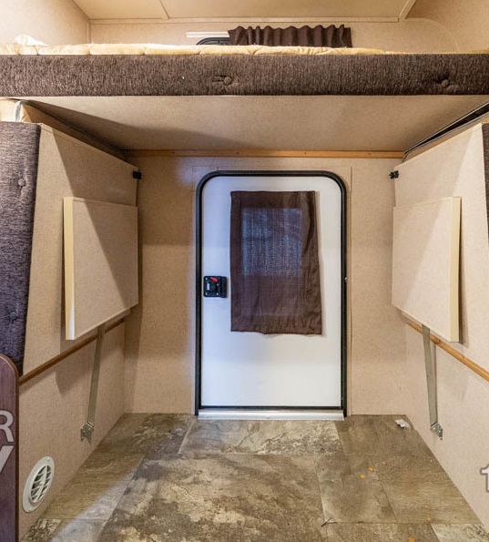 Interior view of an RV rental showing a bunk bed, main entry door, and fold-down side tables.. Jayco Jay Feather Ultra Lite 2015