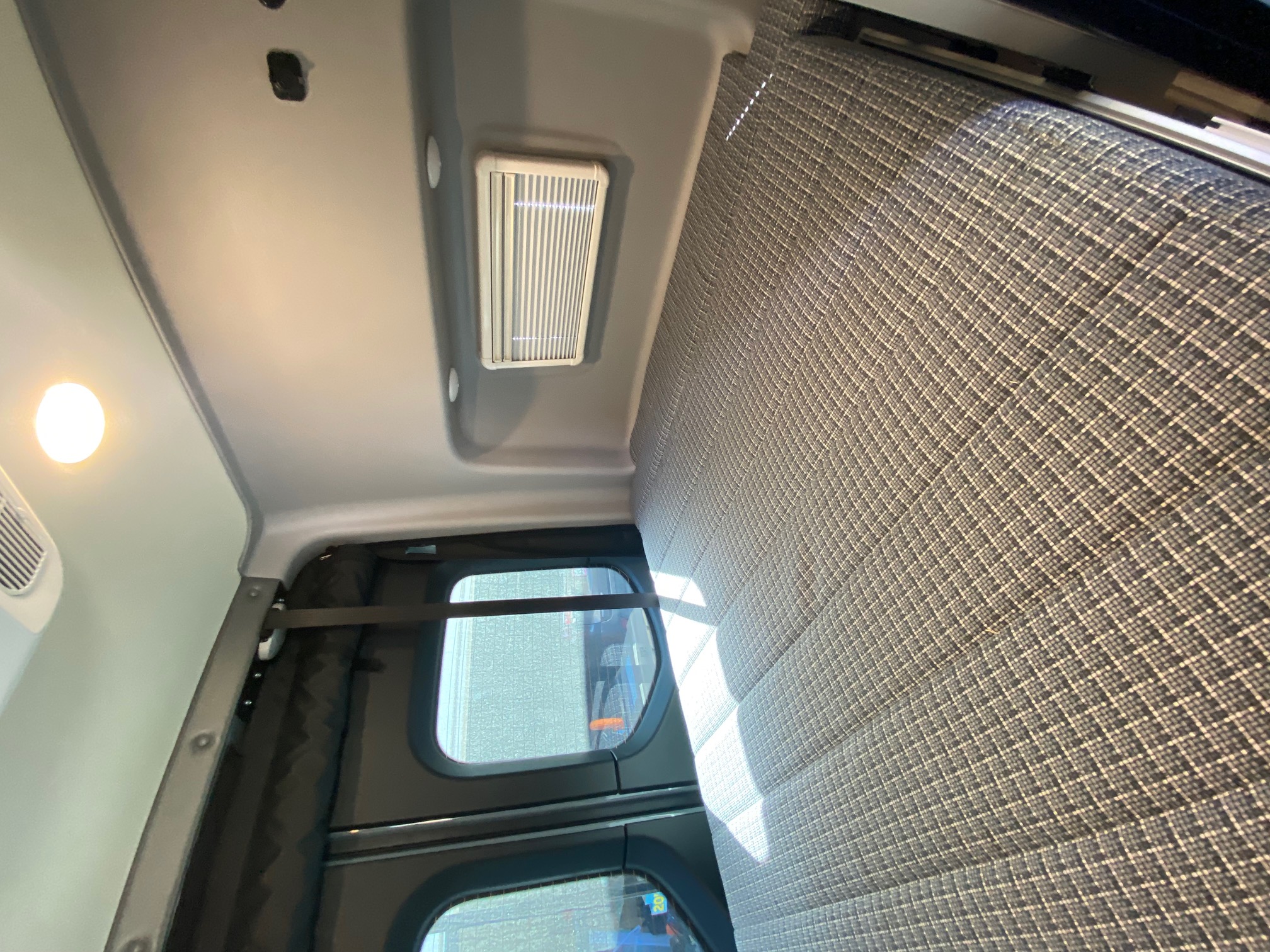 Inside an RV rental: view of the ceiling with light & vent, plus a patterned fabric wall and privacy windows.. Winnebago Revel 2022