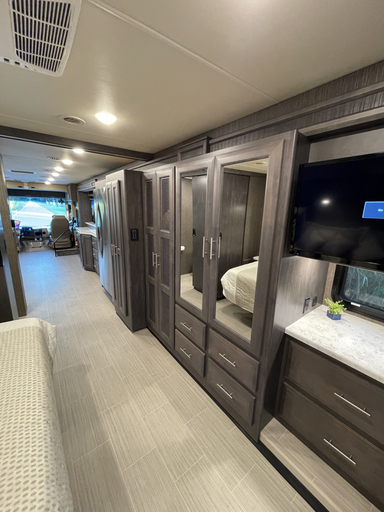 Modern RV rental interior: dark wood cabinetry, mirrored closets, TV, and light tile floor provide stylish comfort for travel.. Thor Challenger 2021