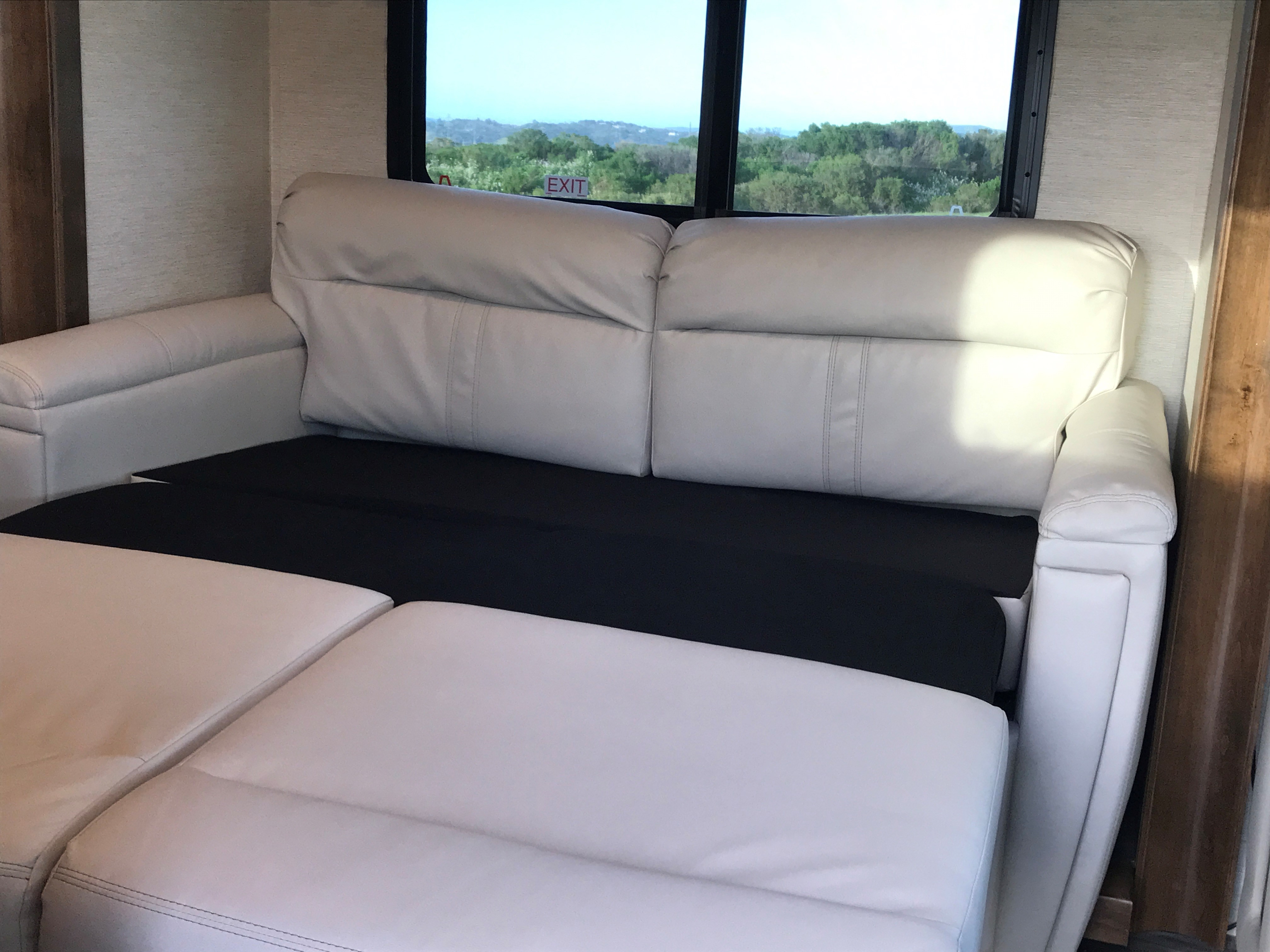 This RV rental features a comfortable, light-colored sofa partially extended, revealing the black base, with a scenic window view.. Wayfarer Wayfarer Motorhome 2020