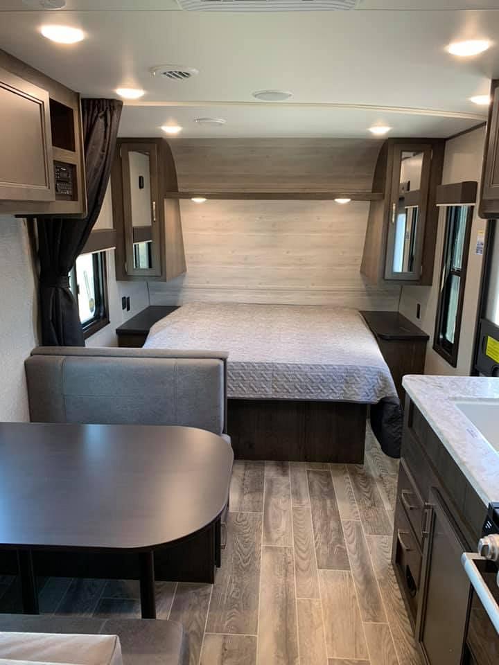 This RV rental interior shows a bed, dining area with booth, and part of the kitchen with a sink.. Jayco Jay Flight 2021