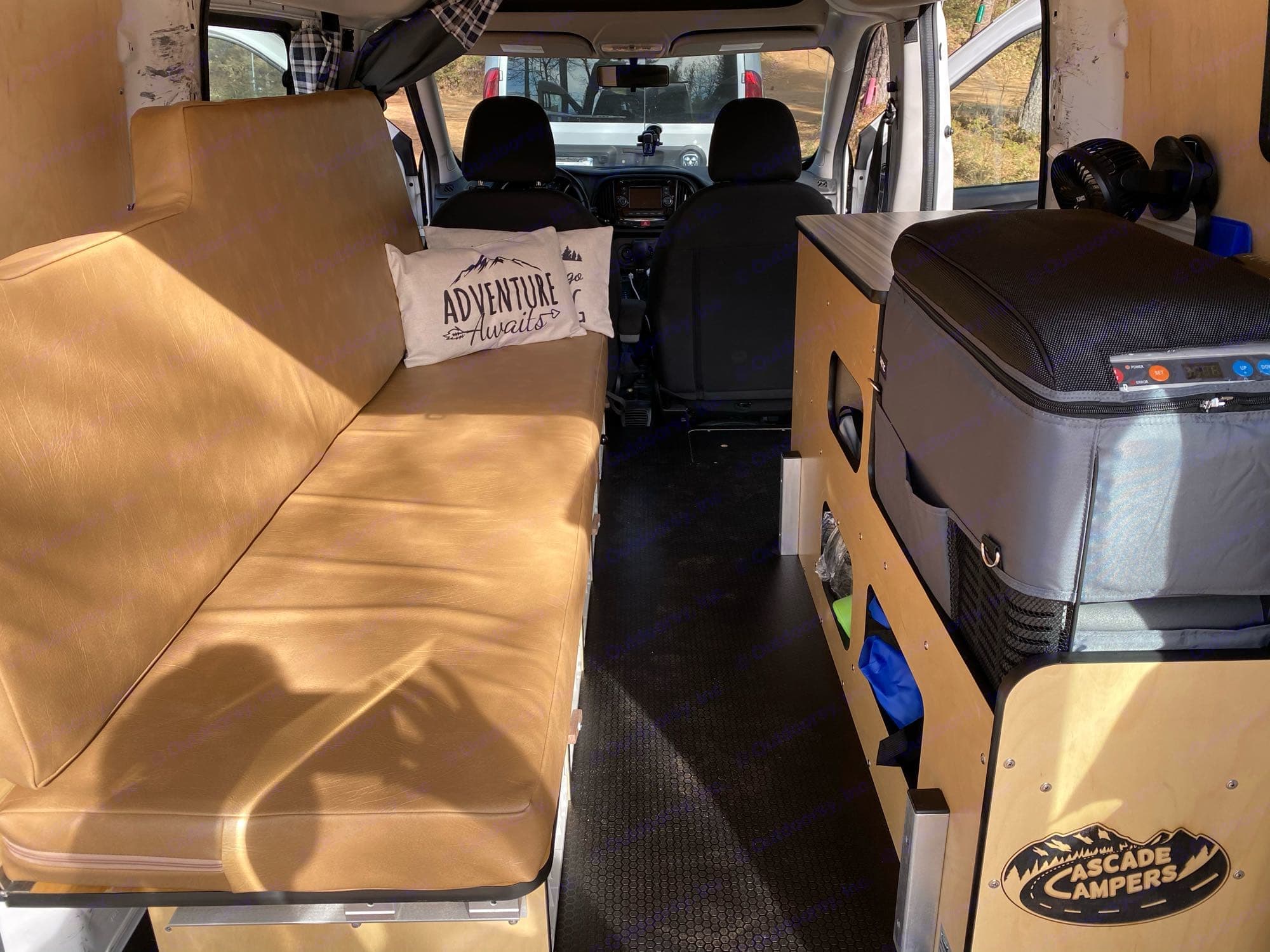 Interior of an rv rental van showing a long bench seat, a portable fridge, and storage. Ready for adventure!. Cascade Campers Ram Promaster City 2020