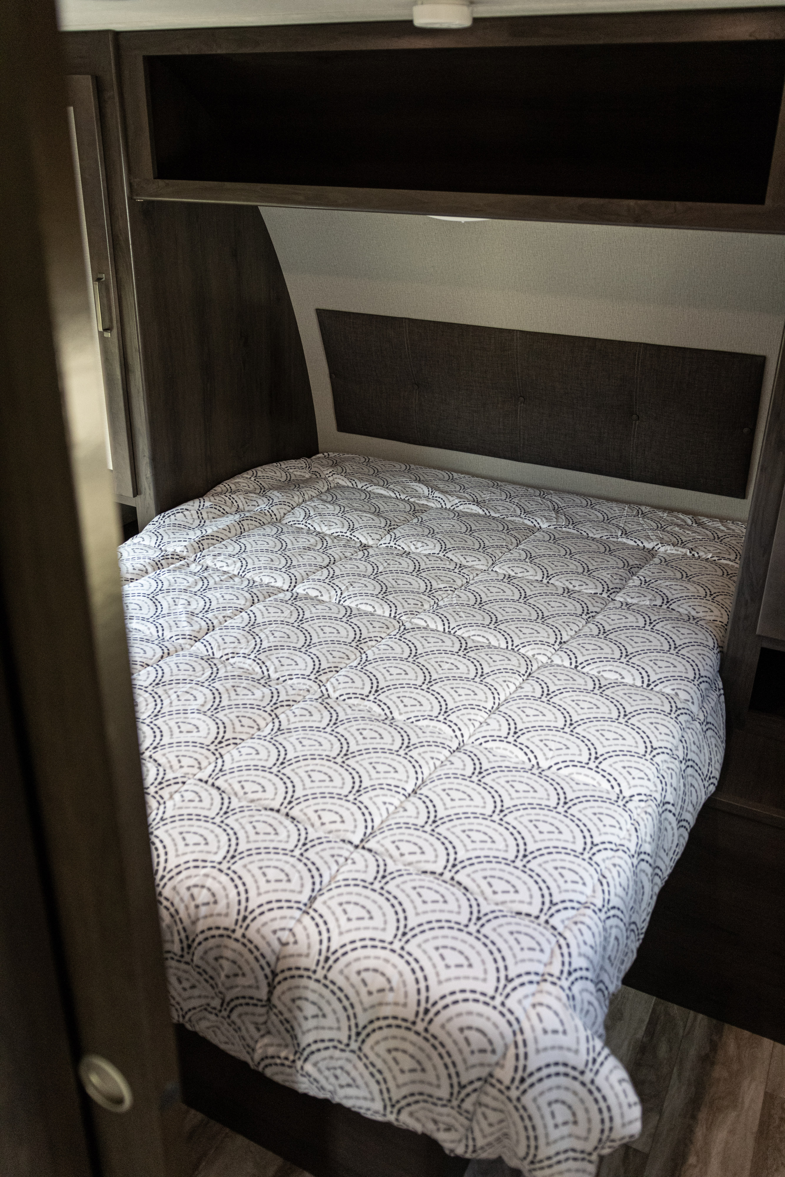 Cozy RV rental bedroom features a patterned comforter, dark wood cabinets, and a fabric headboard for comfortable travel.. Grand Design Other 2022