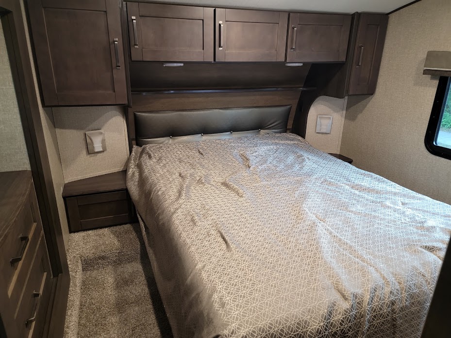 Comfortable RV rental bedroom with a large bed, overhead cabinets, and side nightstands.. Grand Design Reflection 2020