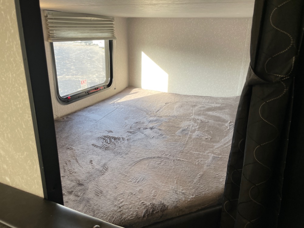 Explore a cozy RV rental sleeping area! This bunk bed features a window with an exit, soft blanket, and privacy curtain.. Forest River Grey Wolf 26DJSE 2022