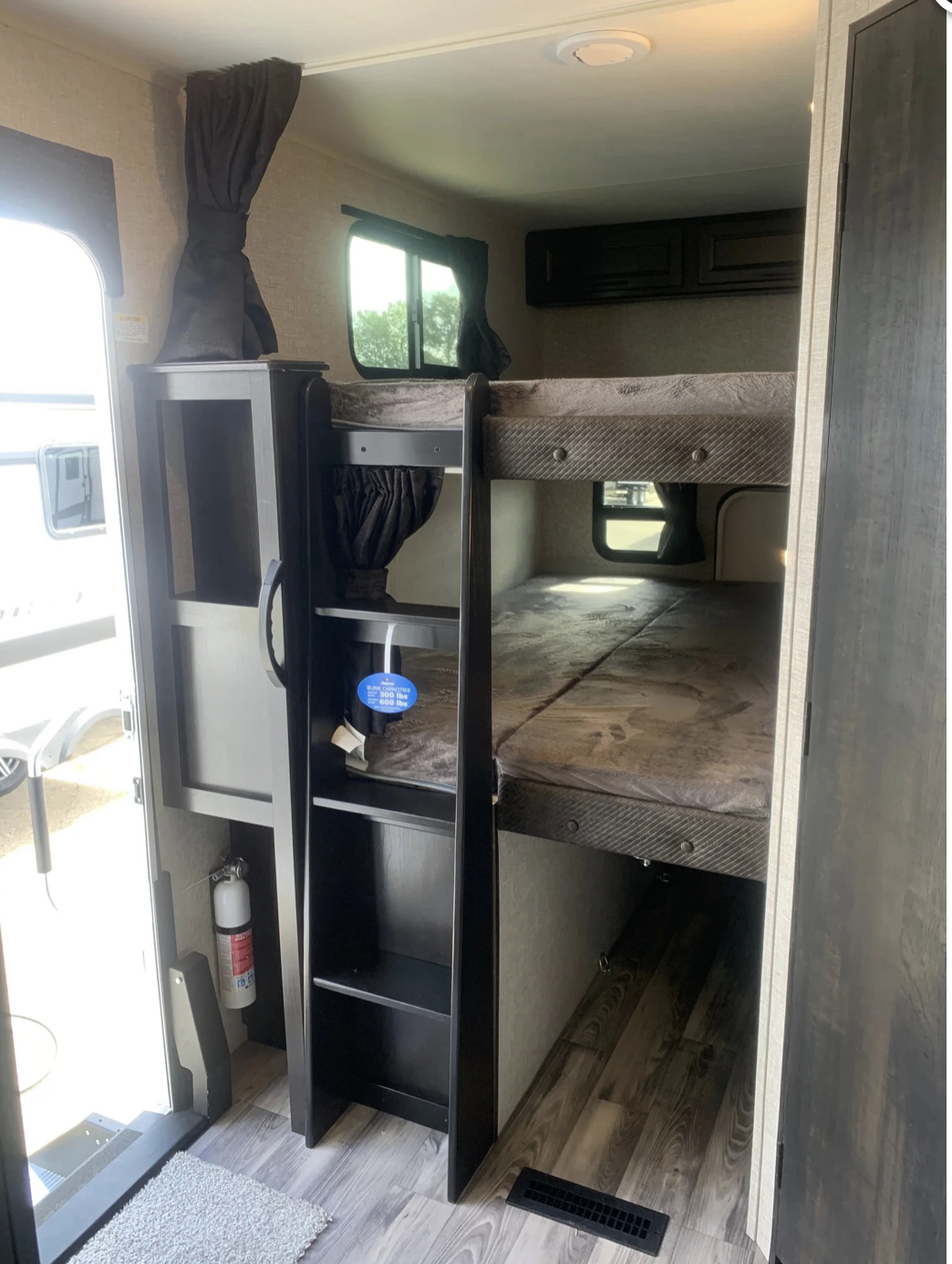Inside an RV rental: cozy bunk beds with a ladder, windows, and a fire extinguisher for safe travels.. Jayco EAGLE 2022