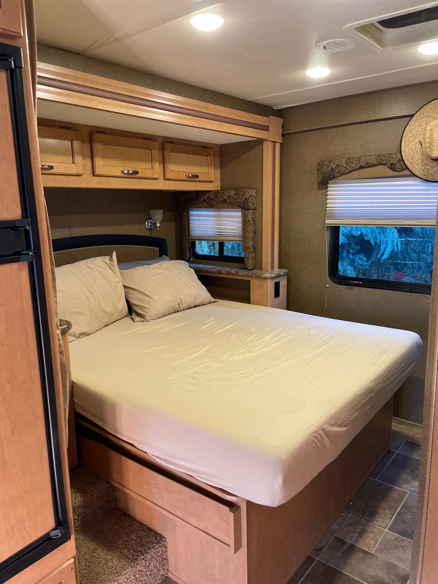 Cozy RV rental bedroom with a comfortable bed, beige linens, overhead storage cabinets, and a window for scenic views on your journey.. Thor Freedom Elite 2017