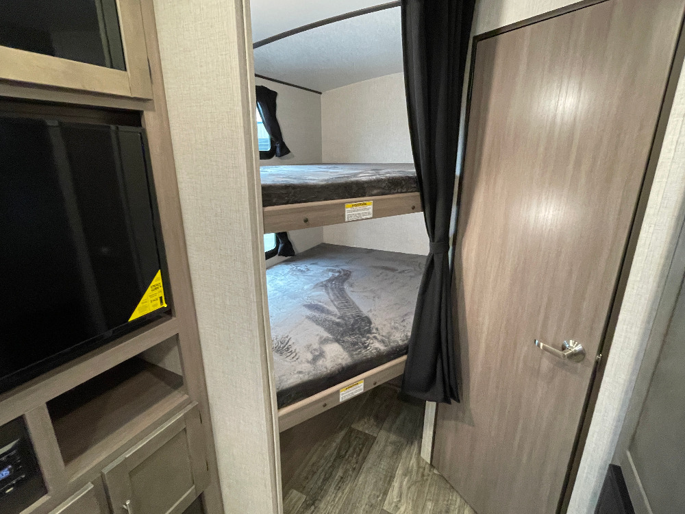 Cozy RV rental interior featuring twin bunk beds, a TV entertainment center, and a privacy door. Ideal for family adventures.. Crossroads Sunset trail 242HB 2022