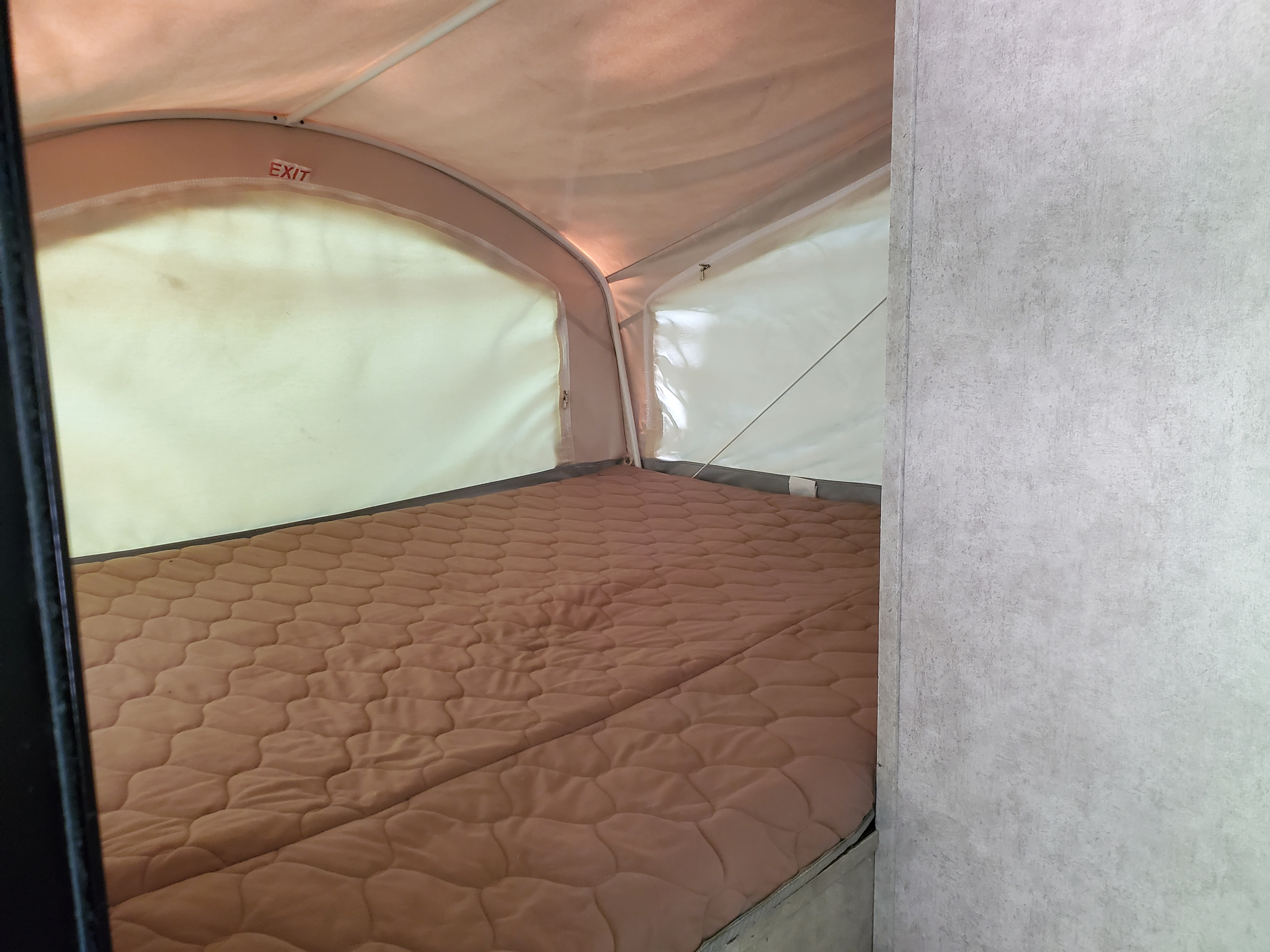 Interior of an RV rental pop-up tent bed, showing a quilted mattress and an "EXIT" sign on the canvas wall.. Coachmen Viking 2018