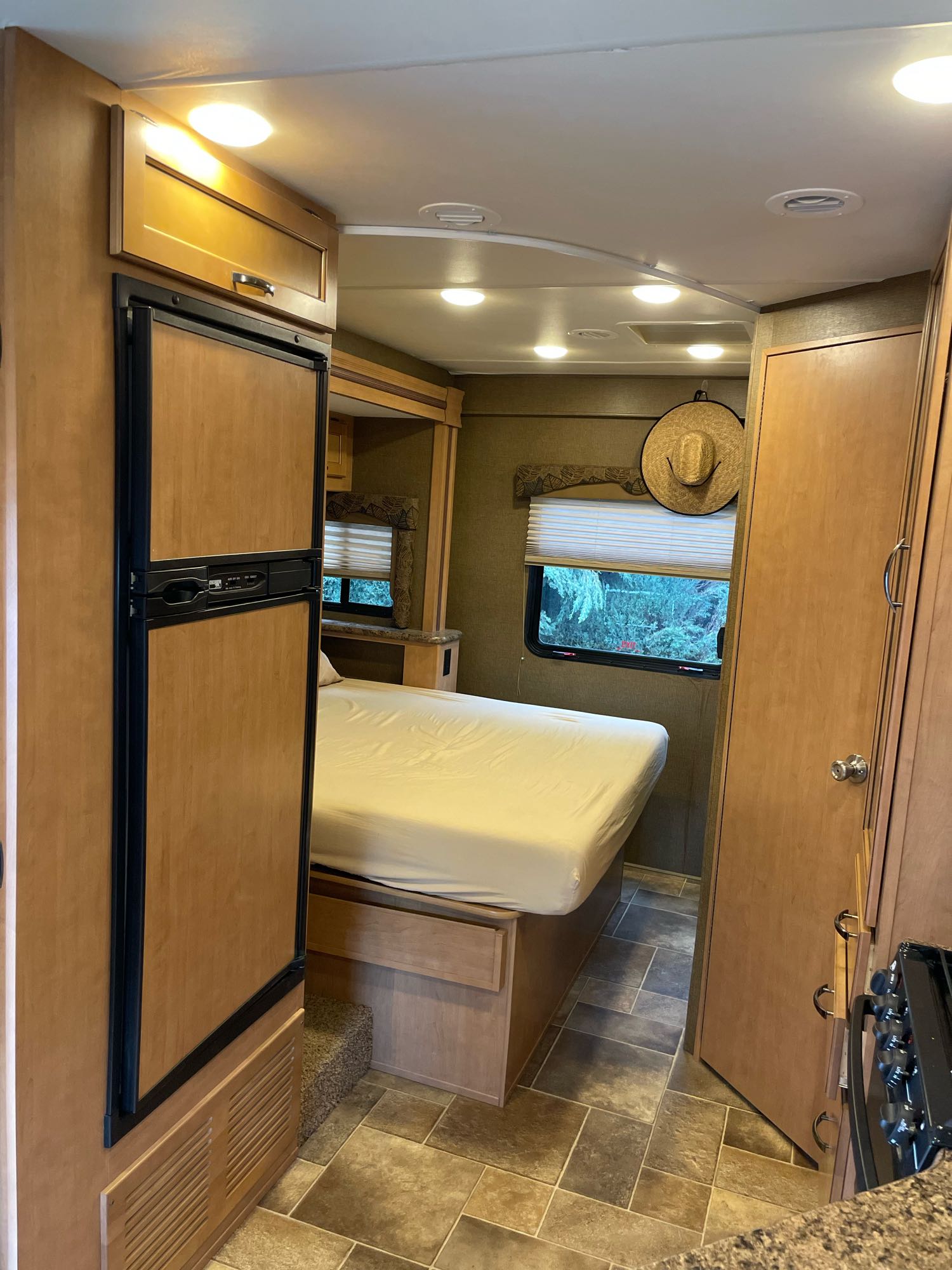 This RV rental features a compact, functional interior with a bed, fridge, and window overlooking trees.. Thor Freedom Elite 2017