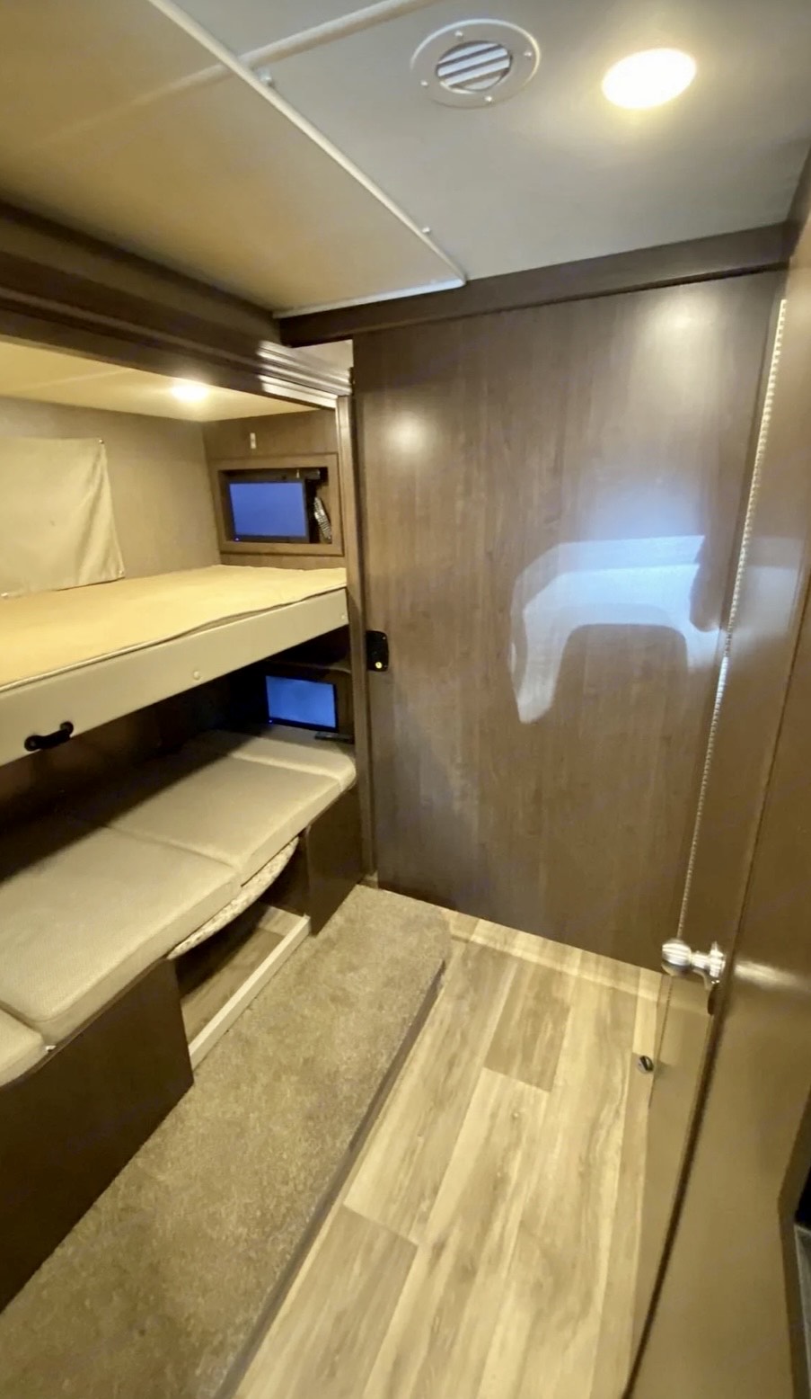 RV rental interior: bunk beds (upper and lower) with personal TVs. Light-colored bedding, carpeted step, and wood-look floor.. Thor Motor Coach Freedom Elite 2019