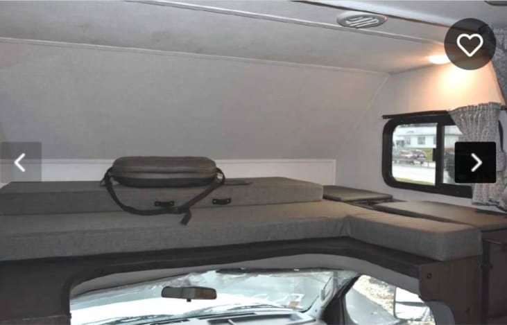 An RV rental's cabover sleeping area with gray cushions, a window, and overhead light. Perfect for travel comfort.. Forest River Sunseeker 2018