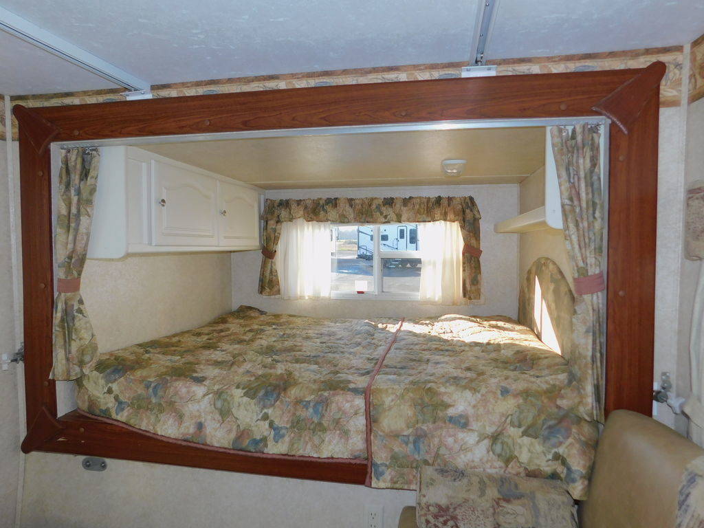 Explore this cozy RV rental interior: a framed bedroom with a comfortable bed, cabinets, and window view.. Keystone RV Outback 2007