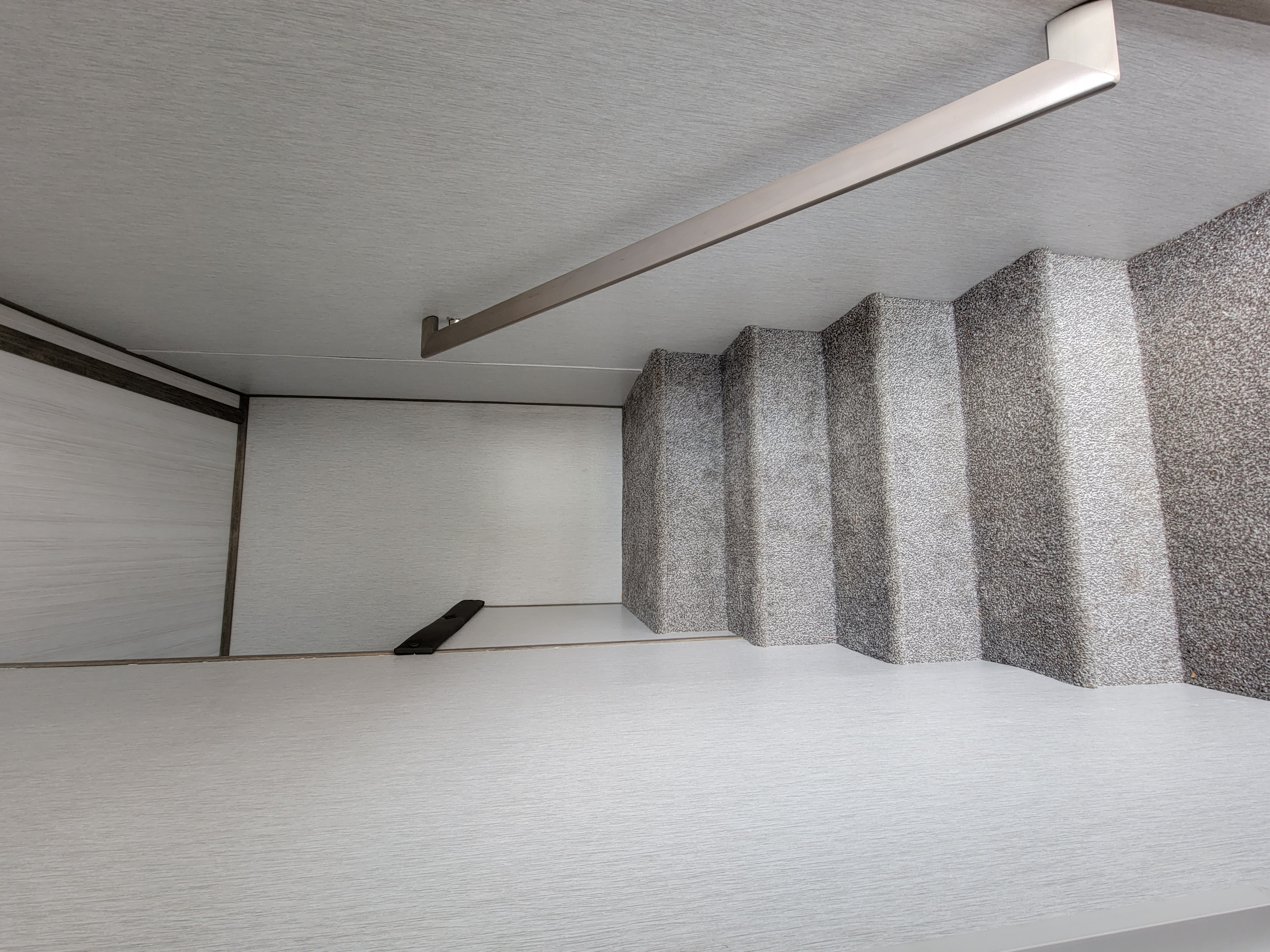 RV rental interior featuring light grey carpeted steps, a light wood-grain wall panel, and a metal bar overhead. Efficient space.. Forest River Heritage Glen 2022
