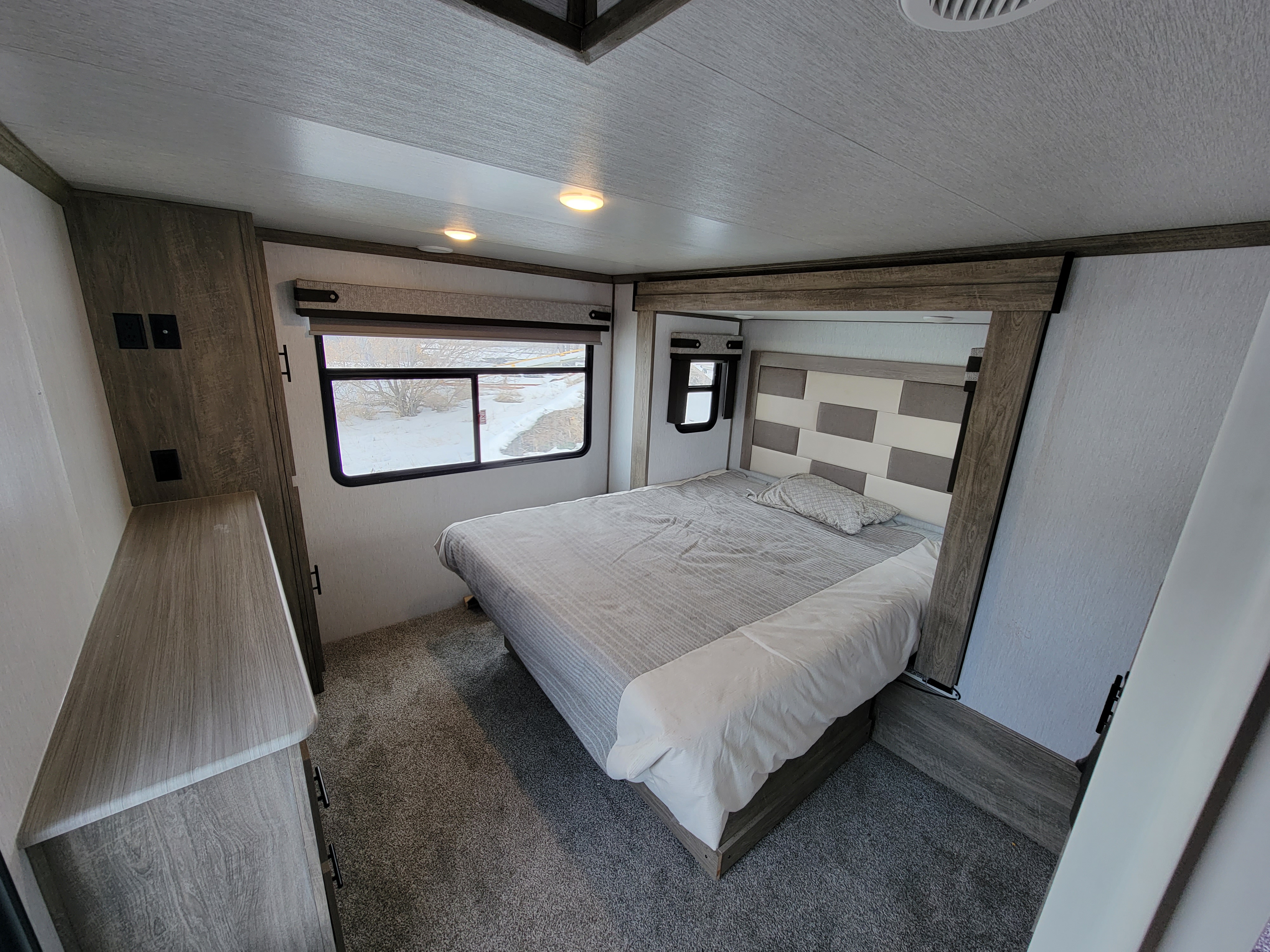 Cozy RV rental bedroom with a modern bed, patterned headboard, and snowy window view.. Forest River Heritage Glen 2022