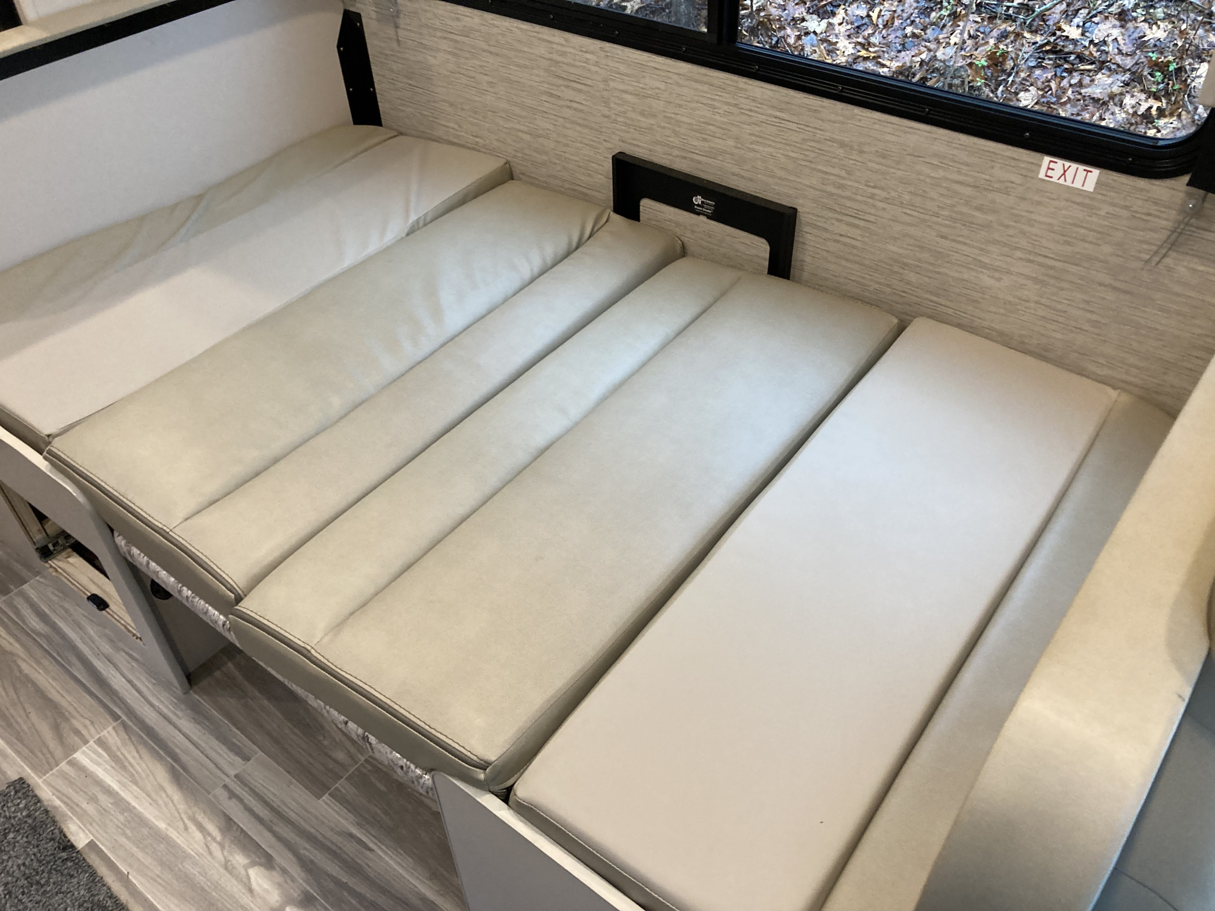 RV rental interior shows a beige convertible seating area or dinette that transforms into a bed, with a window view of foliage.. Thor Freedom Elite 2022
