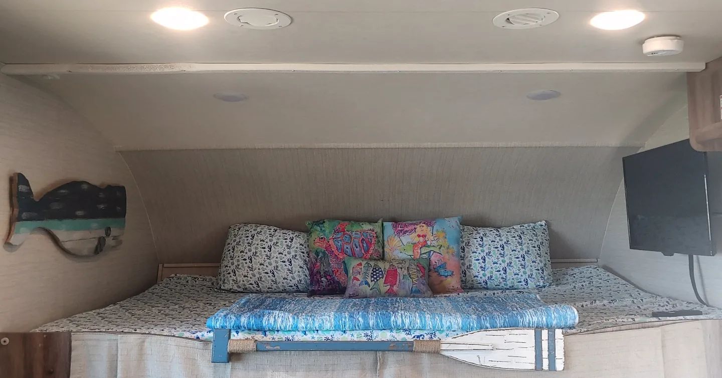 RV rental: A cozy, marine-themed over-cab bed area featuring colorful pillows, a TV, and nautical decor.. Jayco Redhawk 2020