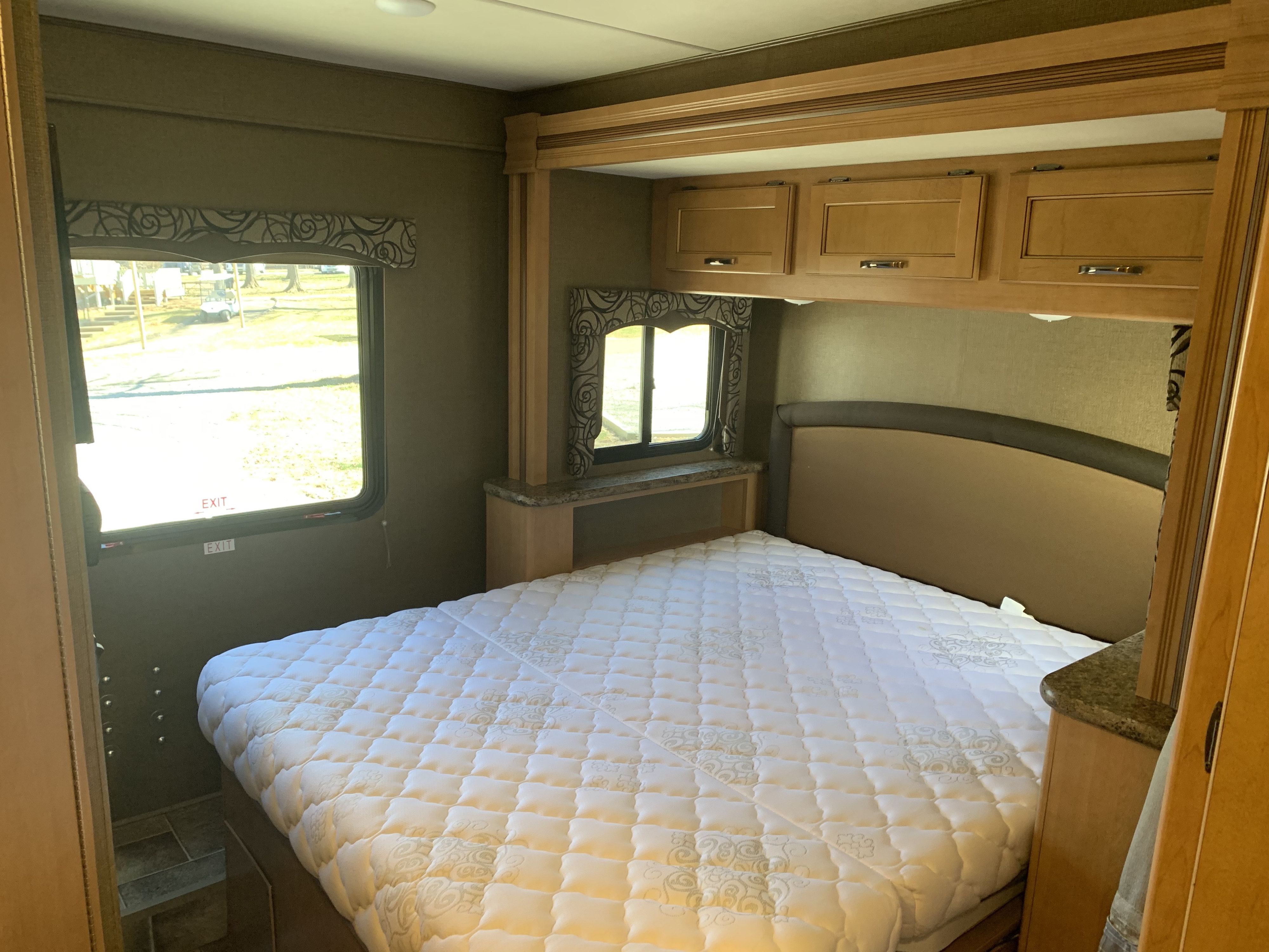 Spacious RV rental bedroom with a large white mattress, overhead cabinets, and dual windows. Ideal for comfortable travel.. Thor Four Winds 2017