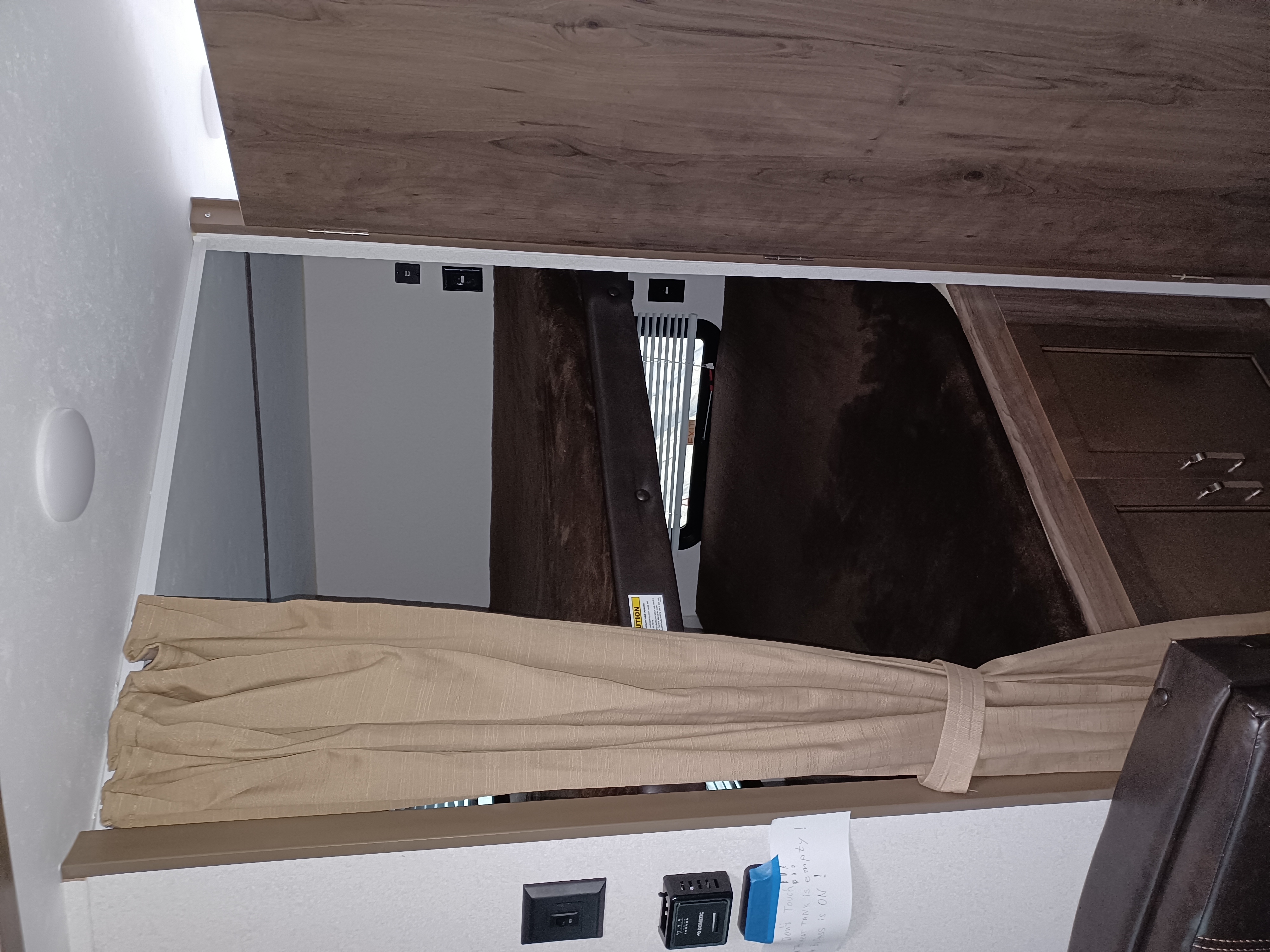 Cozy bunk bed area inside an RV rental, featuring a brown mattress, window, and wall outlets with a note. Perfect for road trips.. Keystone RV Passport Express 2019