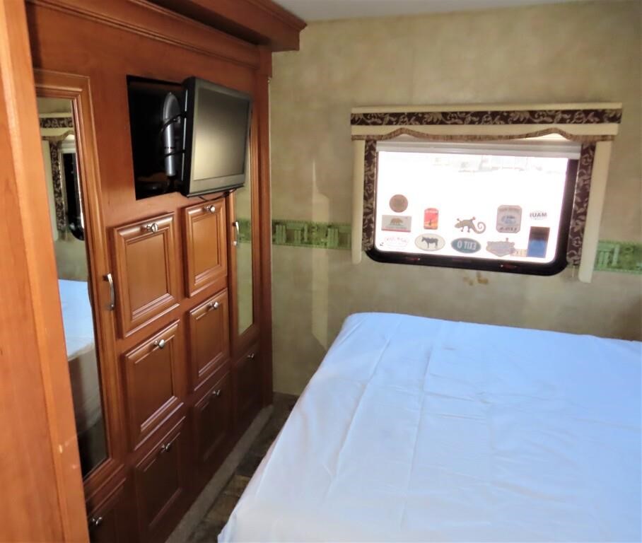 RV rental bedroom with a white-sheeted bed, window, mounted TV, and large wood wardrobe storage. Perfect for travel.. Forest River Other 2011