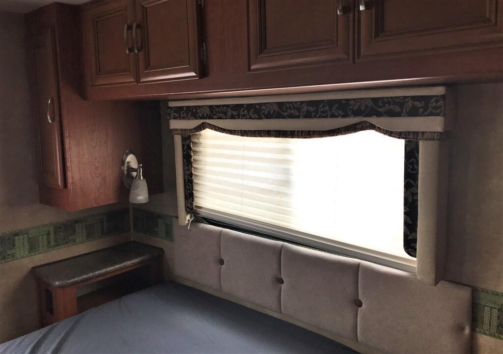Cozy RV rental bedroom featuring a comfortable bed, overhead cabinets, and a bright window with blinds.. Forest River Other 2011