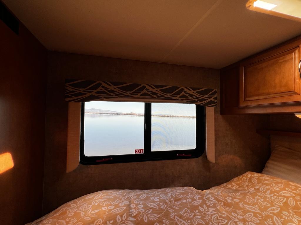 Interior of a cozy RV rental bedroom with a stunning lake view from the window, perfect for travels.. Winnebago Minnie Winnie 2016