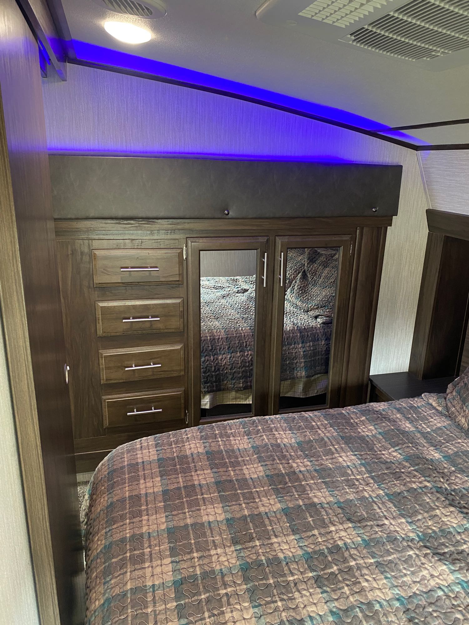 Inside an RV rental: a modern bedroom with plaid bedding, built-in mirrored wardrobe, drawers, and cool blue ambient lighting.. Forest River Cherokee Arctic Wolf 2020