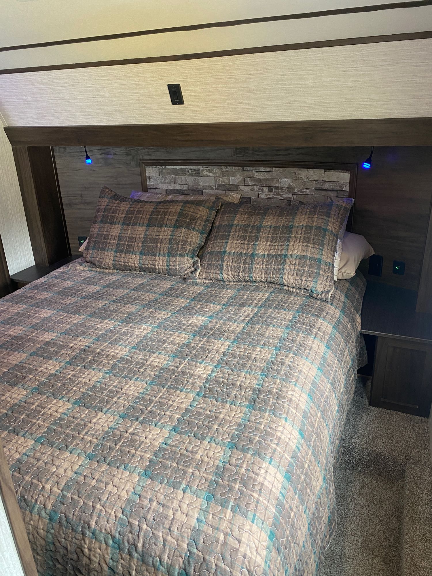 Cozy RV rental bedroom featuring a full bed with plaid bedding, built-in nightstands, and ambient blue lighting.. Forest River Cherokee Arctic Wolf 2020