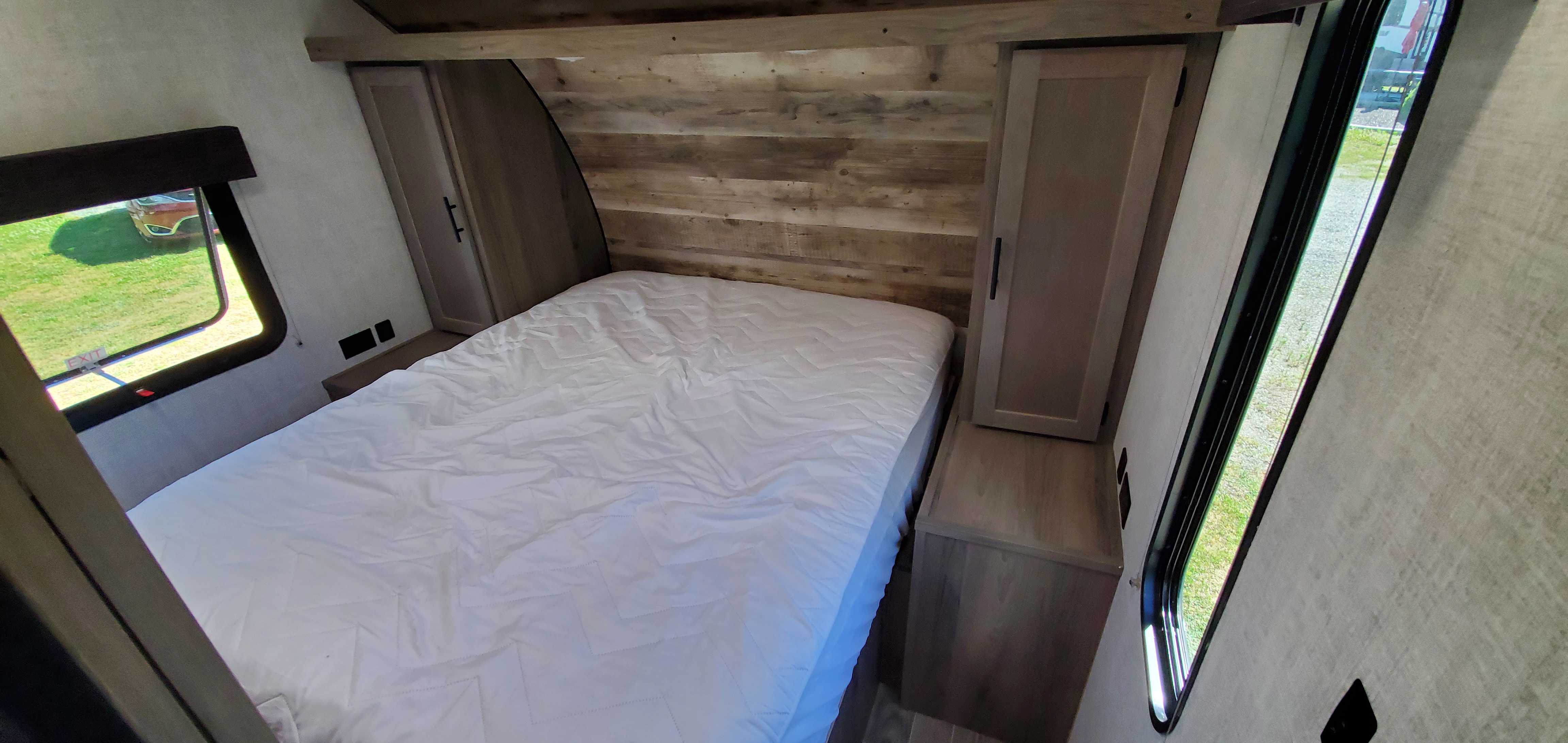 Cozy RV rental bedroom showing a comfortable bed, rustic wood wall, side storage, and windows for natural light.. Gulf Stream Trailmaster 2021