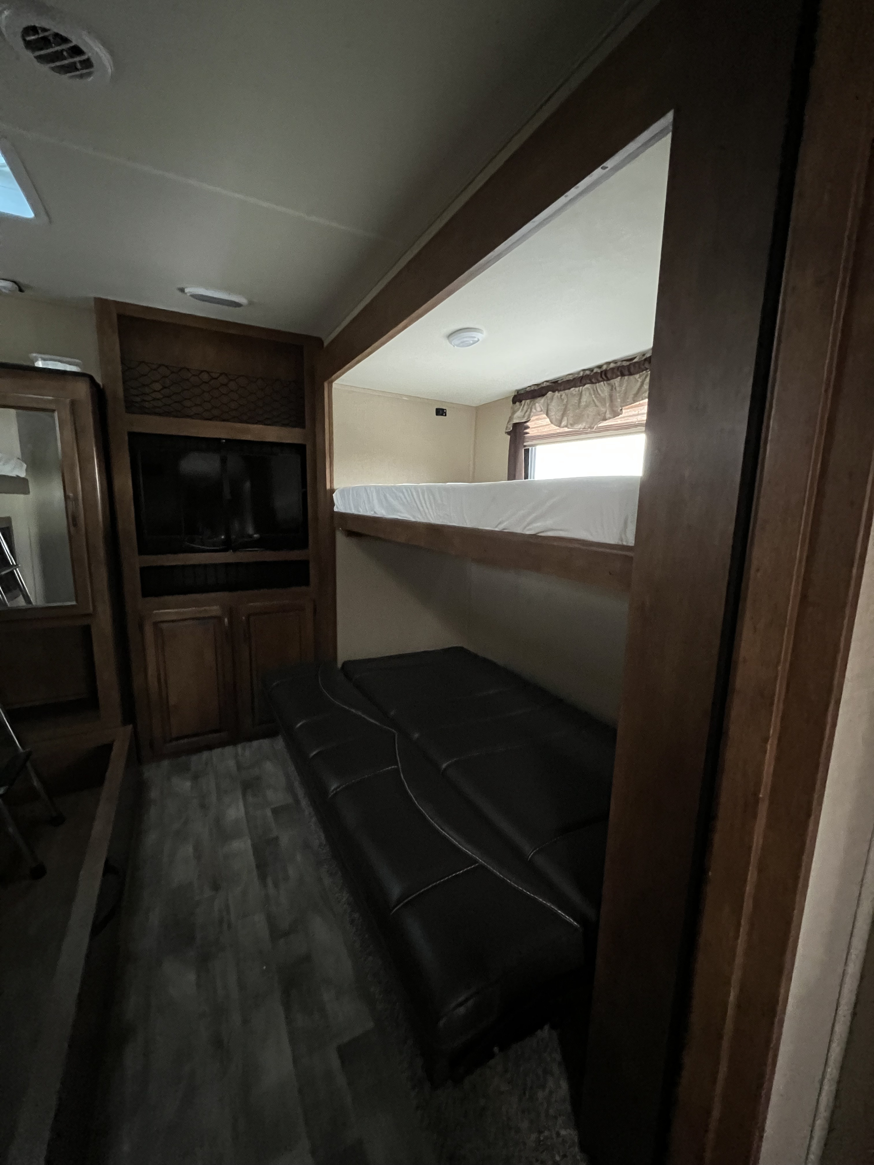 Cozy RV rental interior featuring a living area with TV, dark futon, and a bright bunk bed for comfortable travel.. Grand Design Reflection 2015