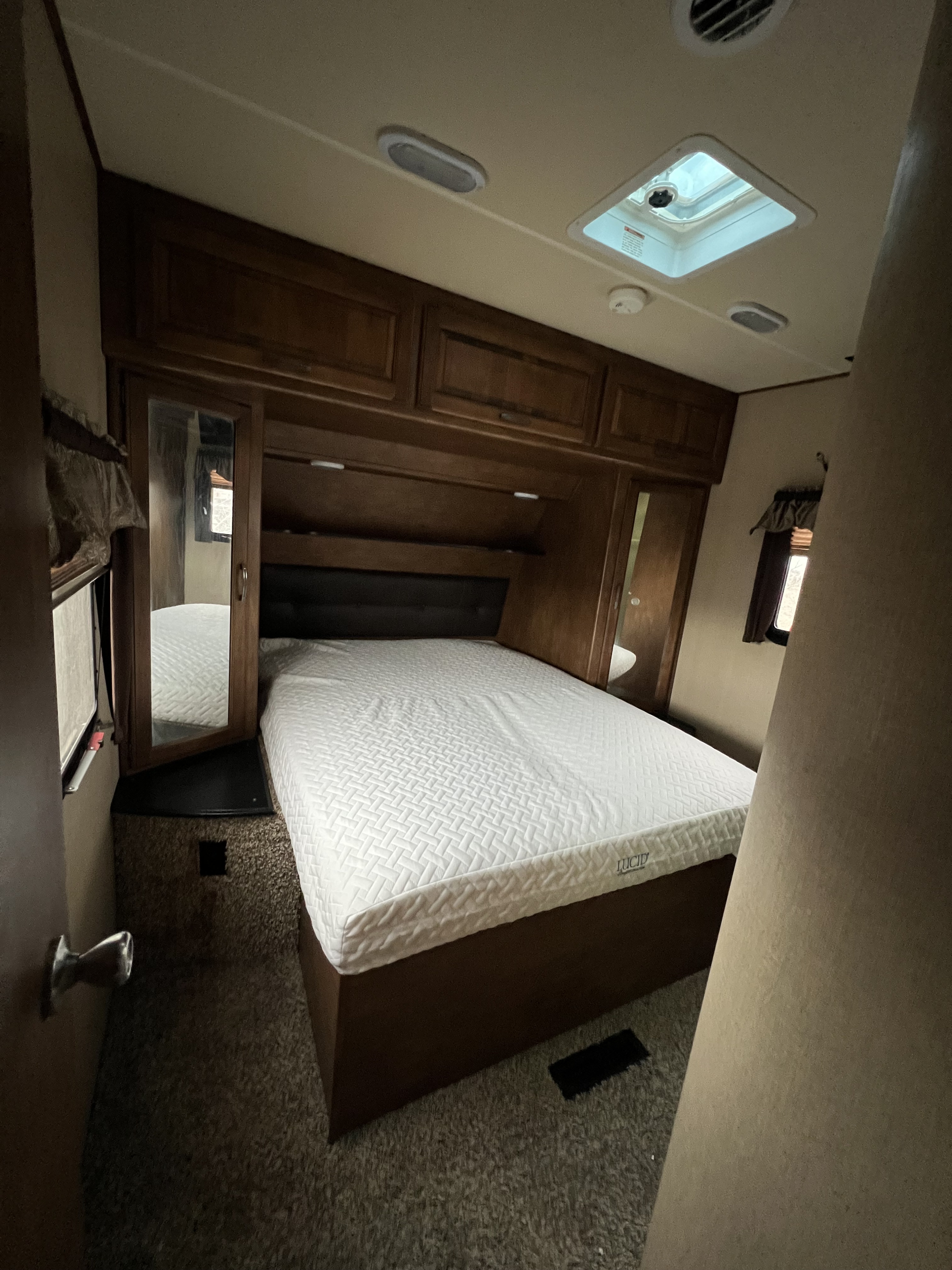 Step into this inviting RV rental bedroom, featuring a comfortable white bed, wooden storage, and a ceiling skylight.. Grand Design Reflection 2015