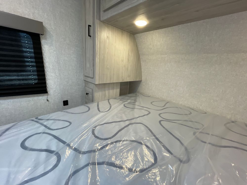 Inside an RV rental: a clean, compact bedroom with a new mattress and overhead storage, ready for travel.. East to West Silver Lake 2022