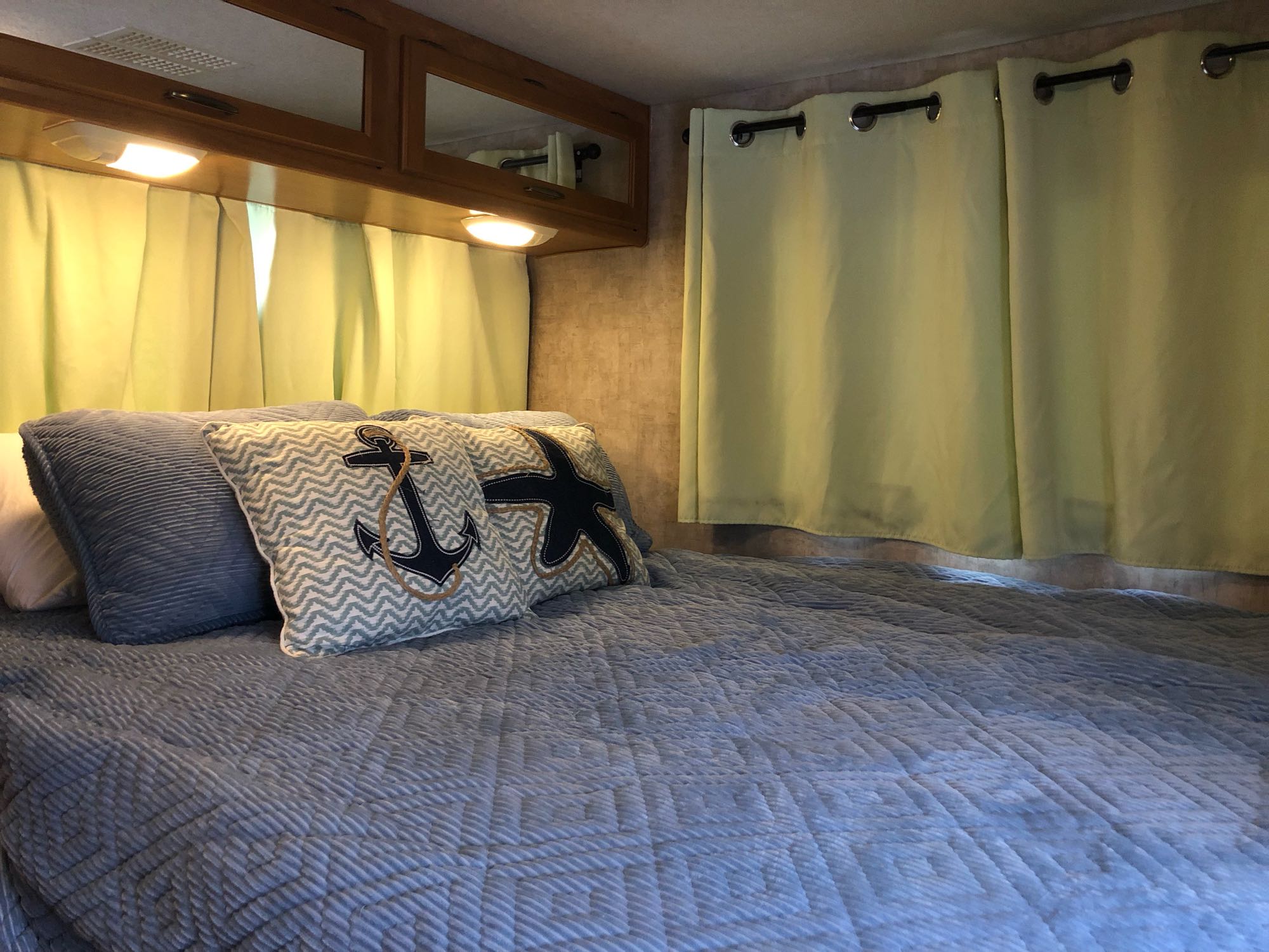 Cozy RV rental bedroom for travel, with blue bedding, nautical pillows, and light green curtains.. Fleetwood Other 2007